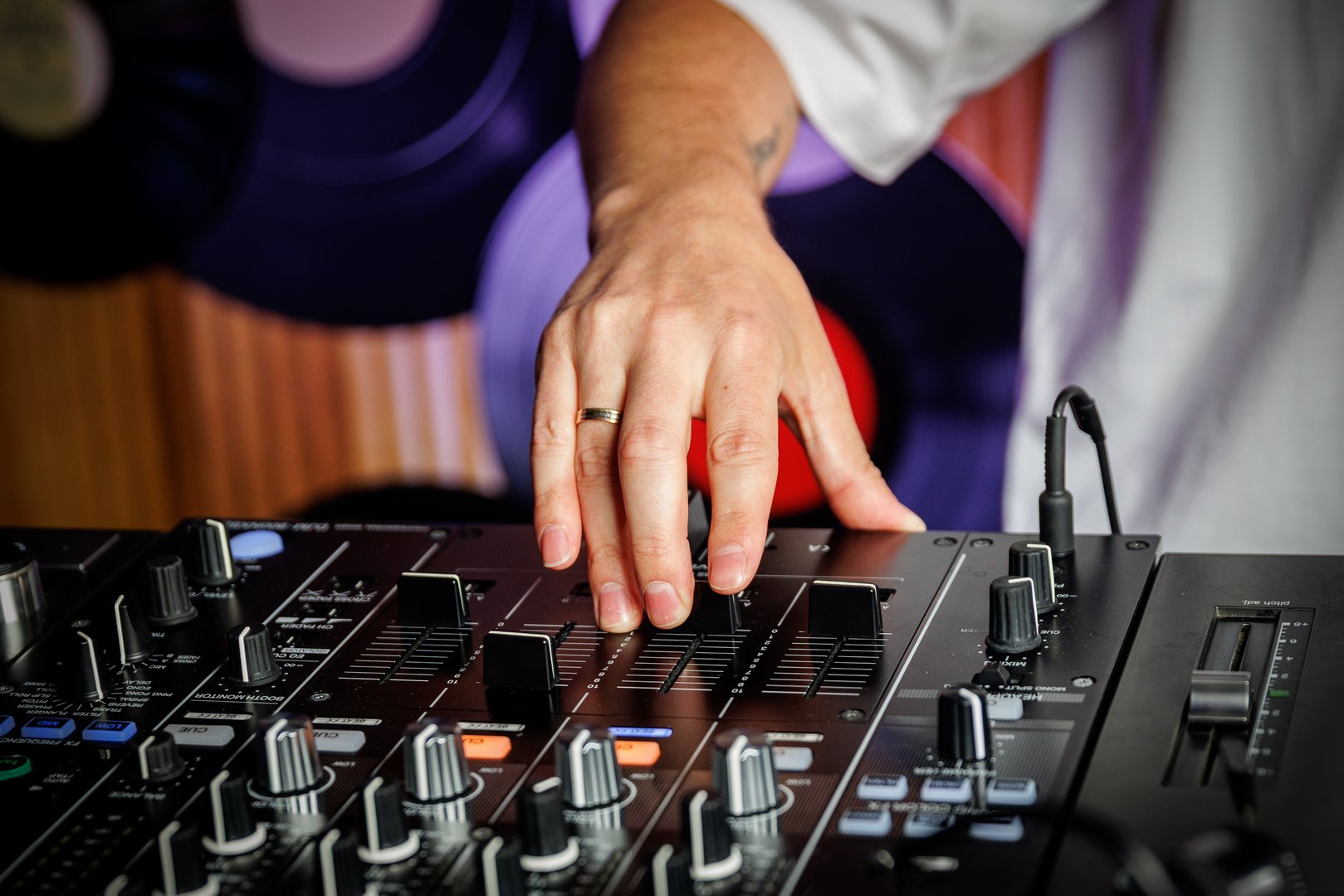 Close-up of DJ hand adjusting knobs and sliders on professional audio mixer during music event or party.