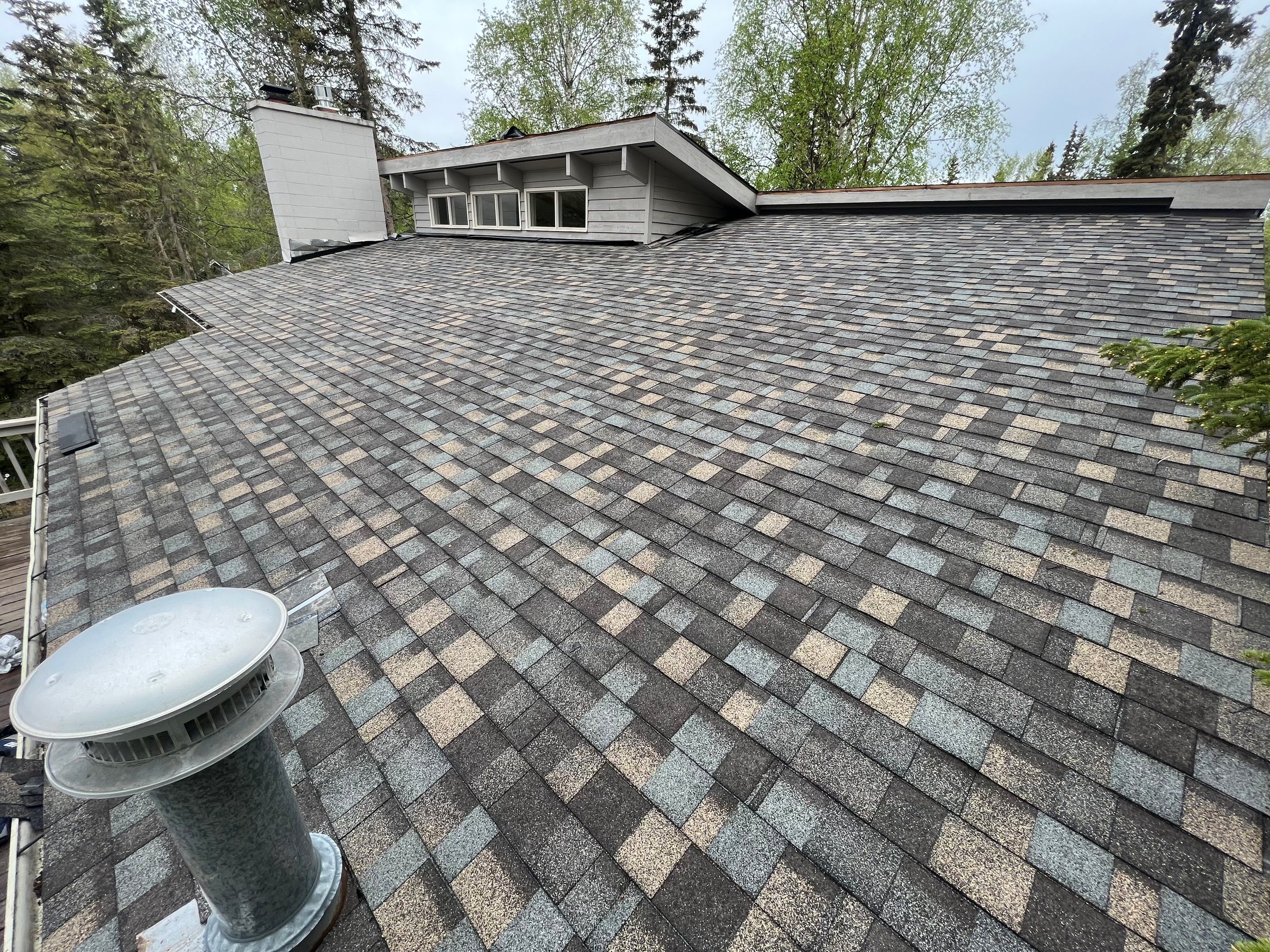 Roofing project Anchorage Alaska - newly installed asphalt shingle roof with chimney and surrounding trees showcasing quality roofing services