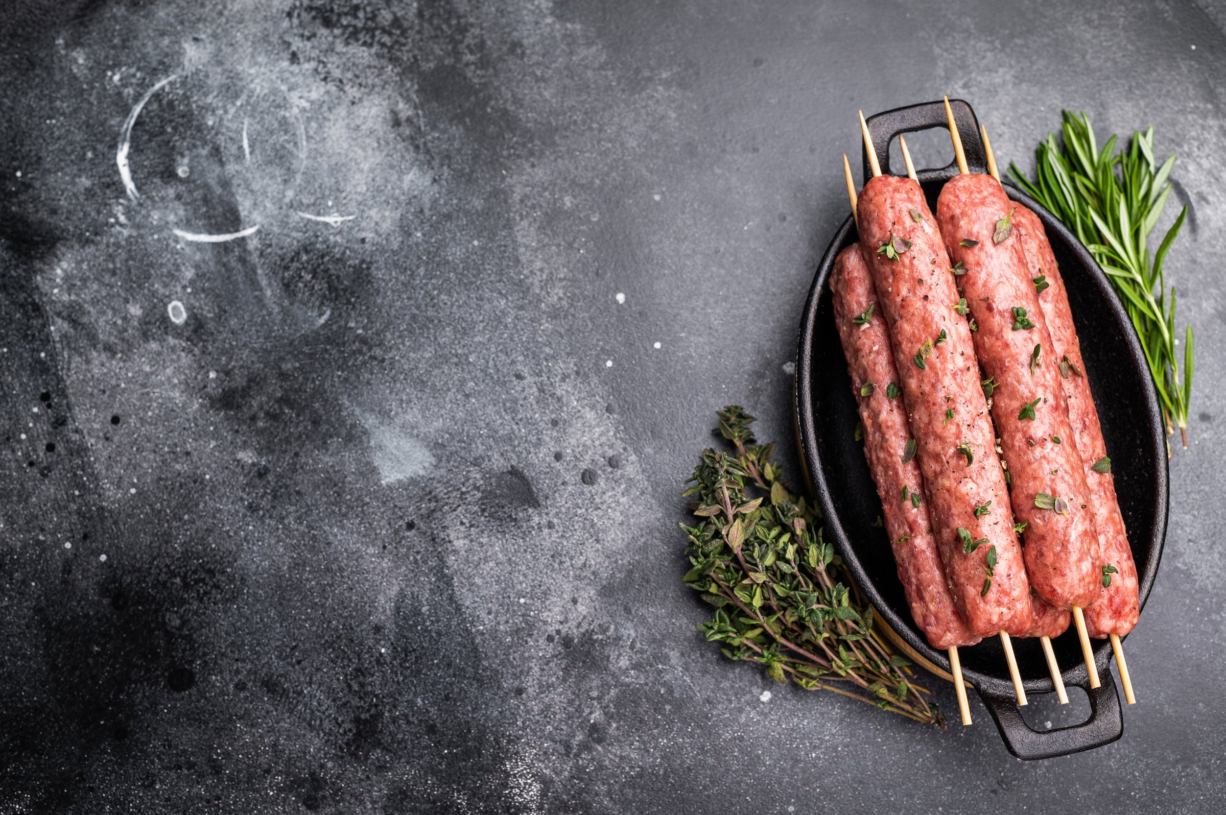 Raw shish kebab, arabic kofta kofte kebab from mince lamb and beef meat on Skewer. black background. top view.