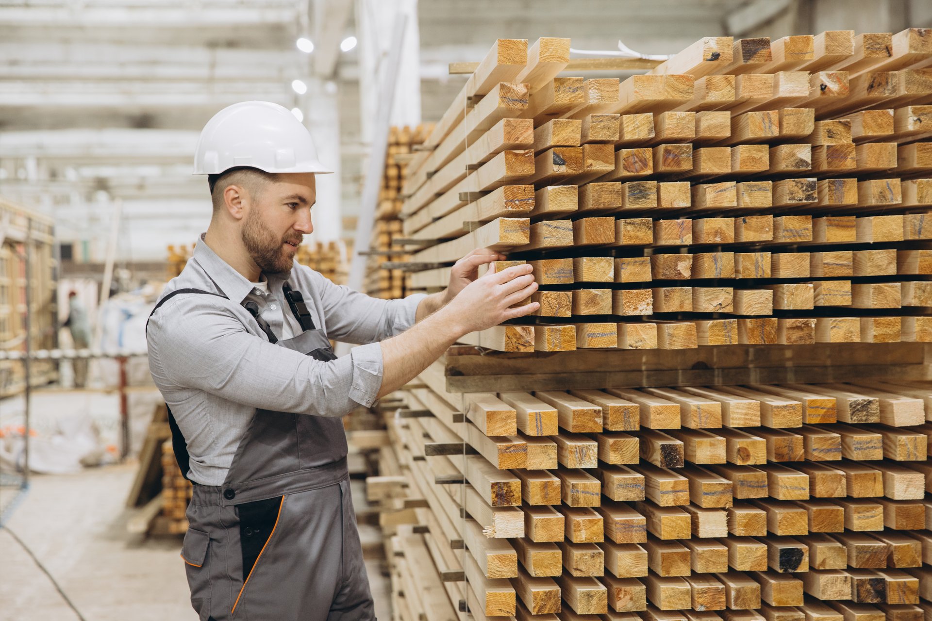 Carpenter wearing safety helmet checking quality of wooden planks in a timber warehouse, working in the modular building industry