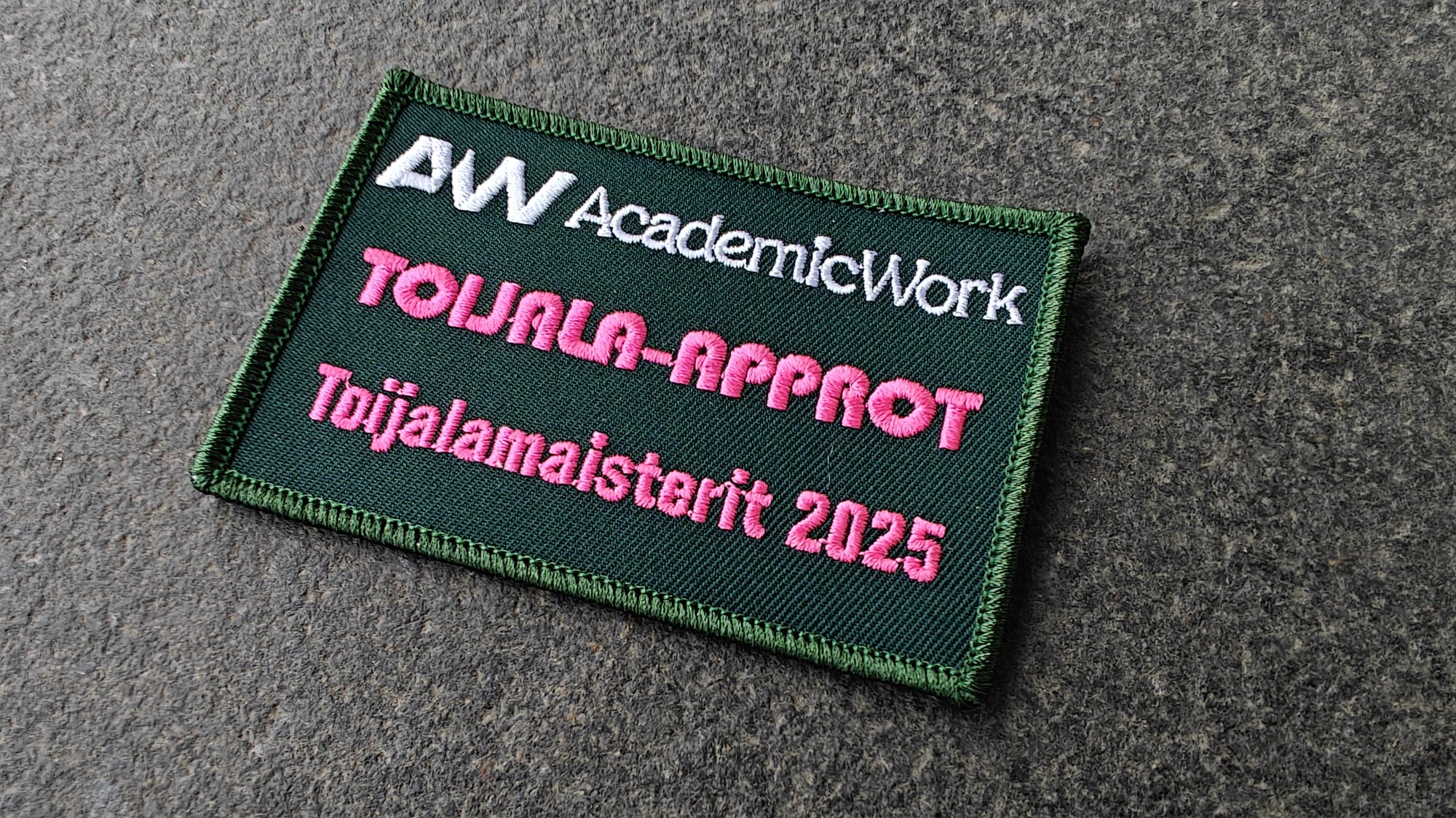 A green embroidered patch with AW Academic Work, TOIJALA-APPROT, and Toijalamaisterit 2025 in white and pink text.