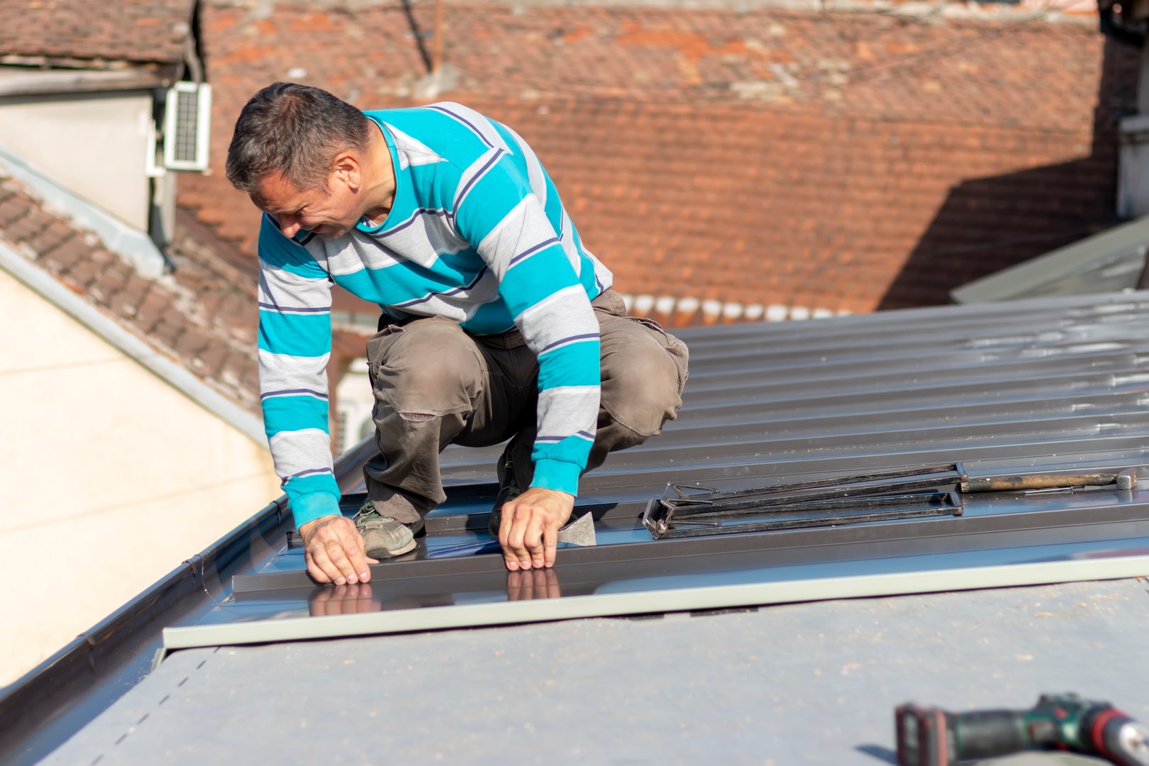 Roofer assembles sheet metal on the roof. Construction workers - installation assembly of new roof. Roofing tools.