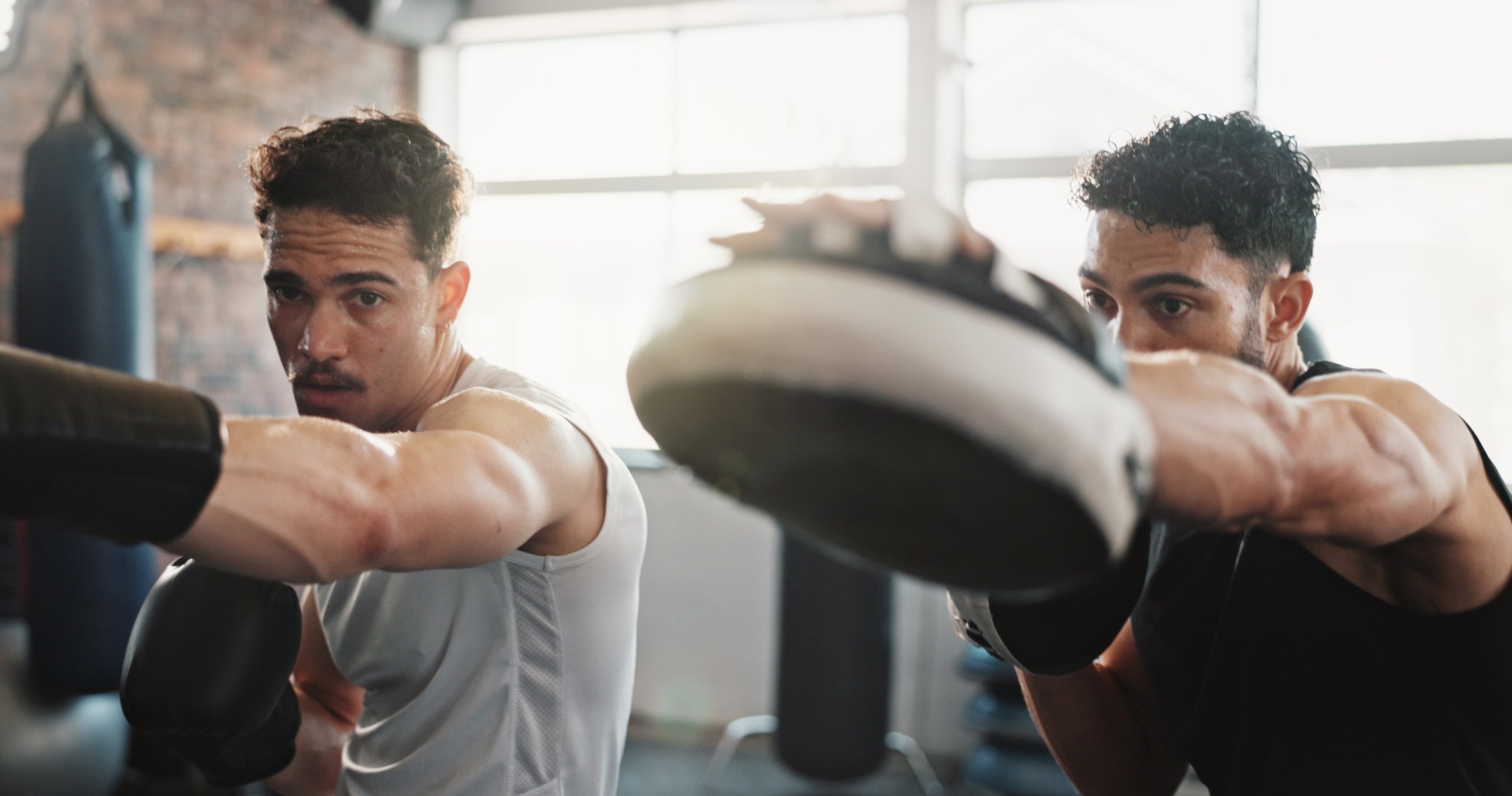 Men, personal trainer or boxer with practice at gym for training, exercise or workout together. Male person, fitness instructor or coach helping fighter with gloves for self defense at health club