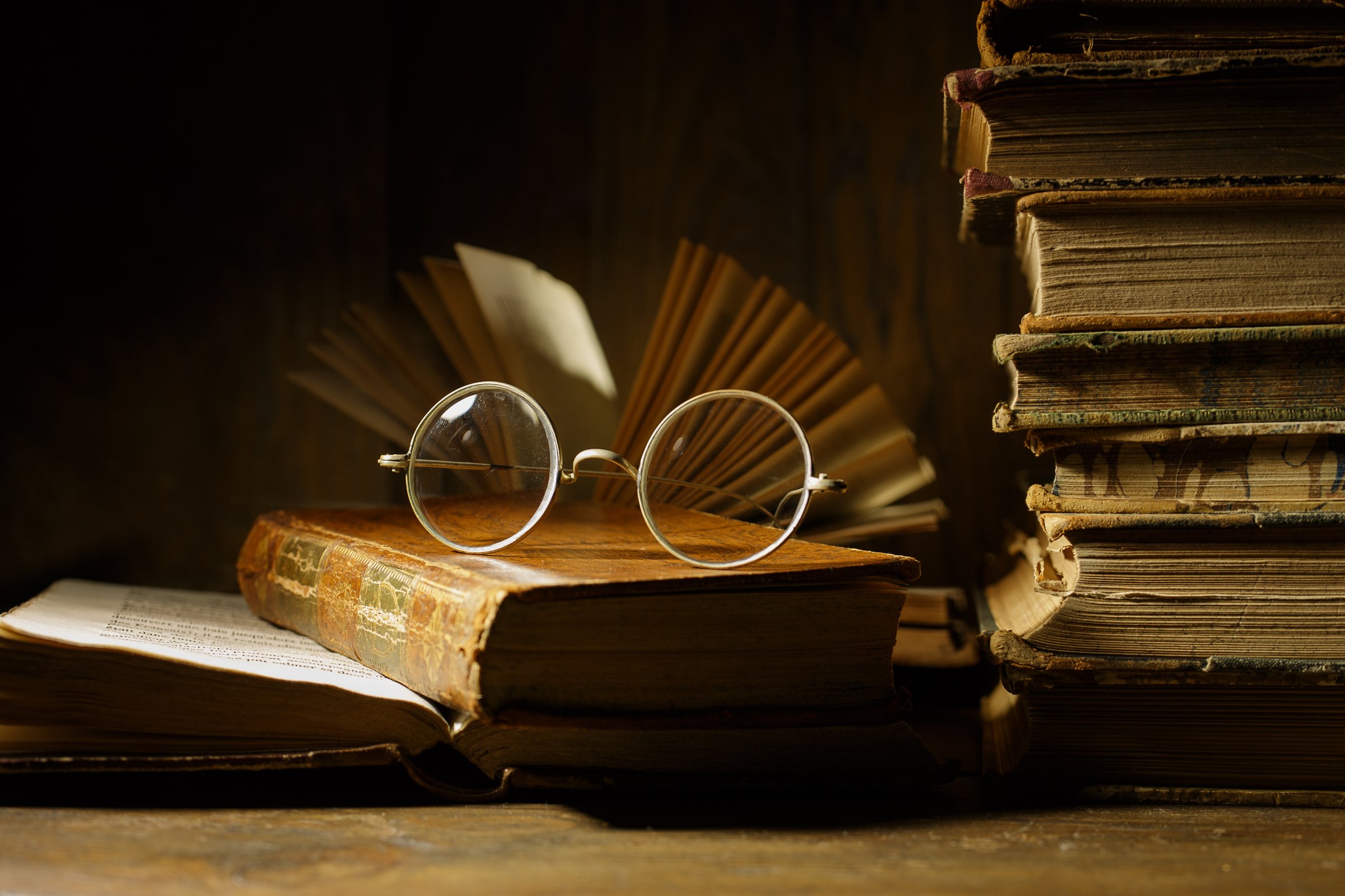 Old round glasses on antique book. Stack of old books on old wooden table. Vintage still life. Education concept