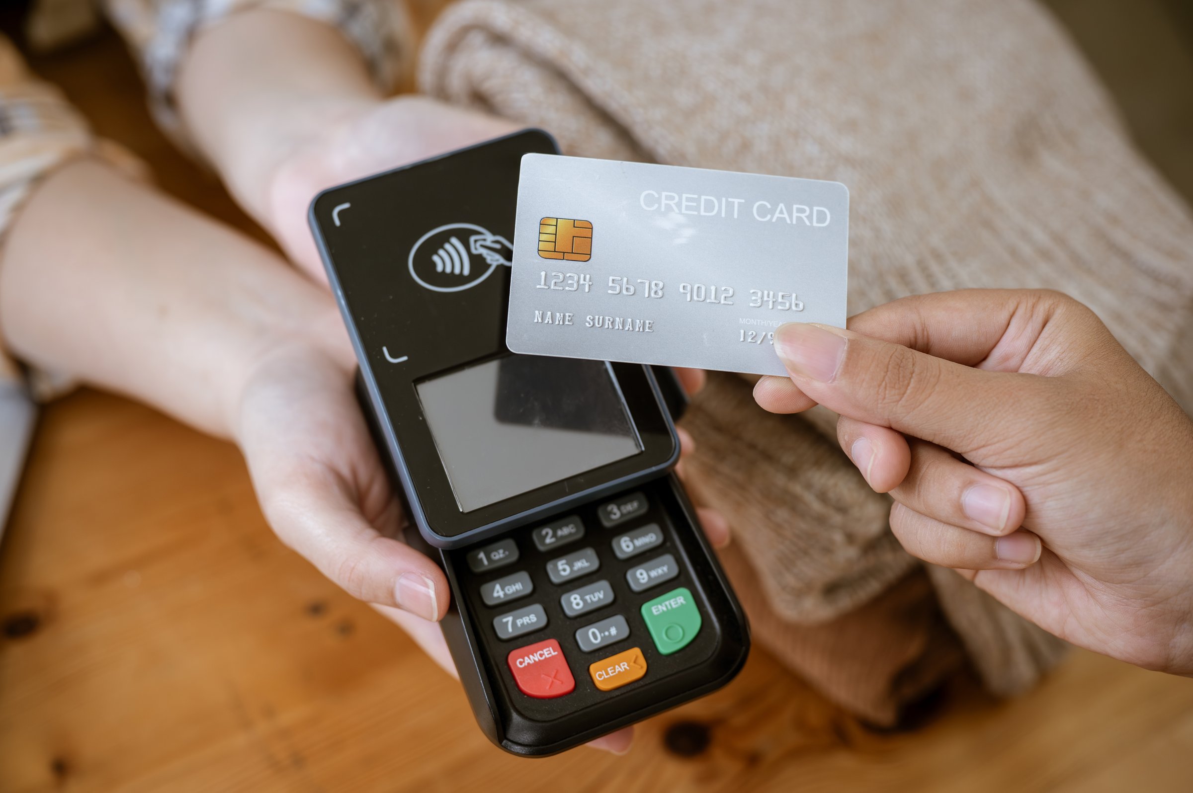 A close-up image of a customer tapping her credit card with a payment terminal or credit card machine at a cashier in a clothing store. cashless payment, card reader, electronic funds transfer