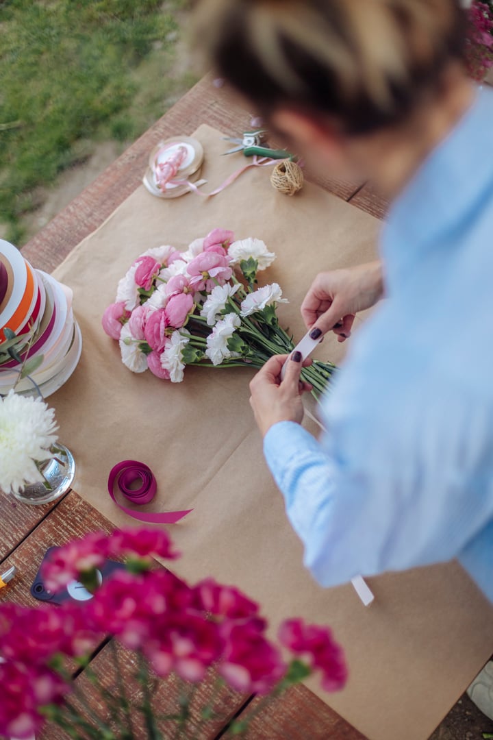 Rear view of a female florist, small business owner, arranging a pink and white bouquet as a custom order in her cozy flower shop.