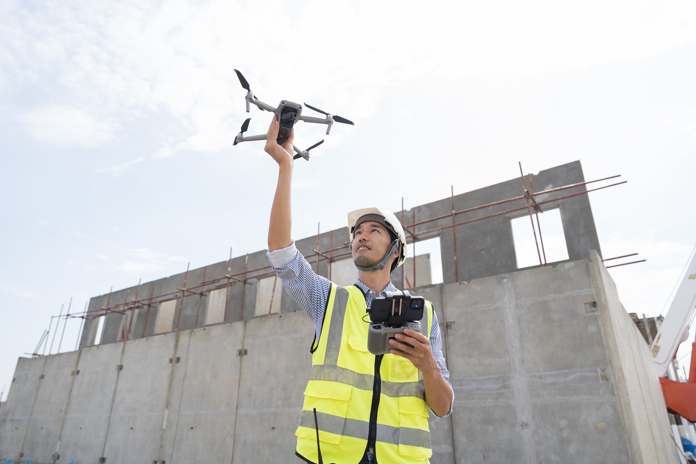 Construction site. Civil engineer. Construction engineer using drone supervising construction work at construction site. Asian engineer working at job site of building