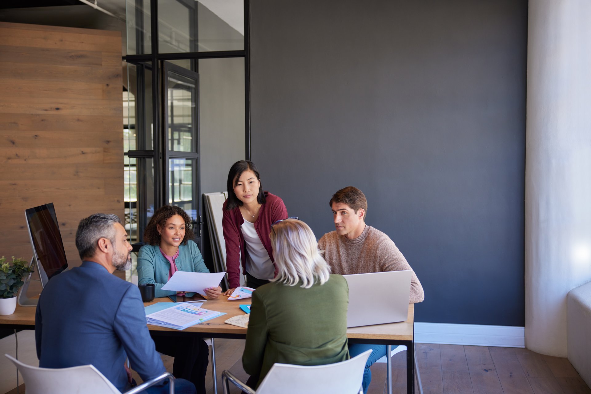 Business team meeting discussing  strategies around a conference table. Colleagues collaborating on a project in a modern office space. Multiethnic businesswomen and mid adult businessmen in a serious team discussion during meeting.