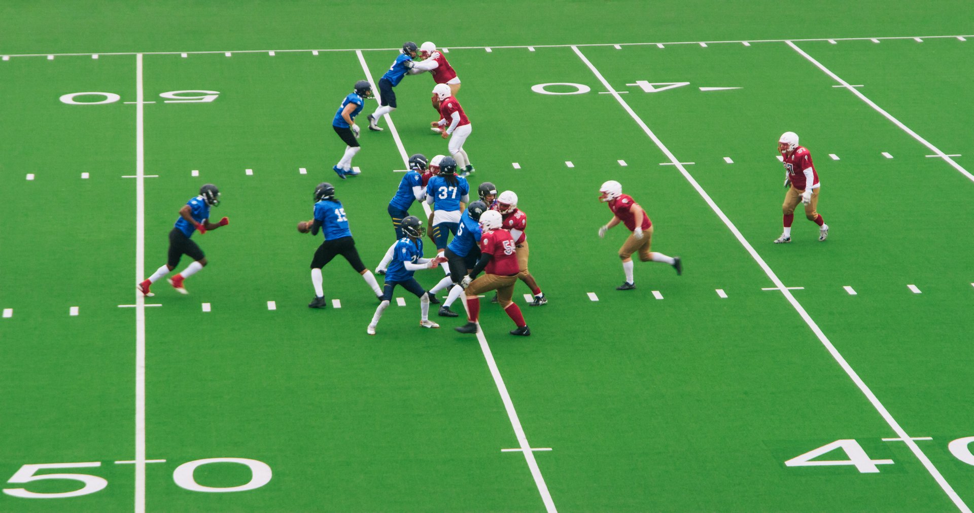 American Football Players Sprinting to Make a Goal. Authentic Gridiron Game on a Big Green Outdoors Field with Markings. Opposing Teams Playing a Championship Tournament Match