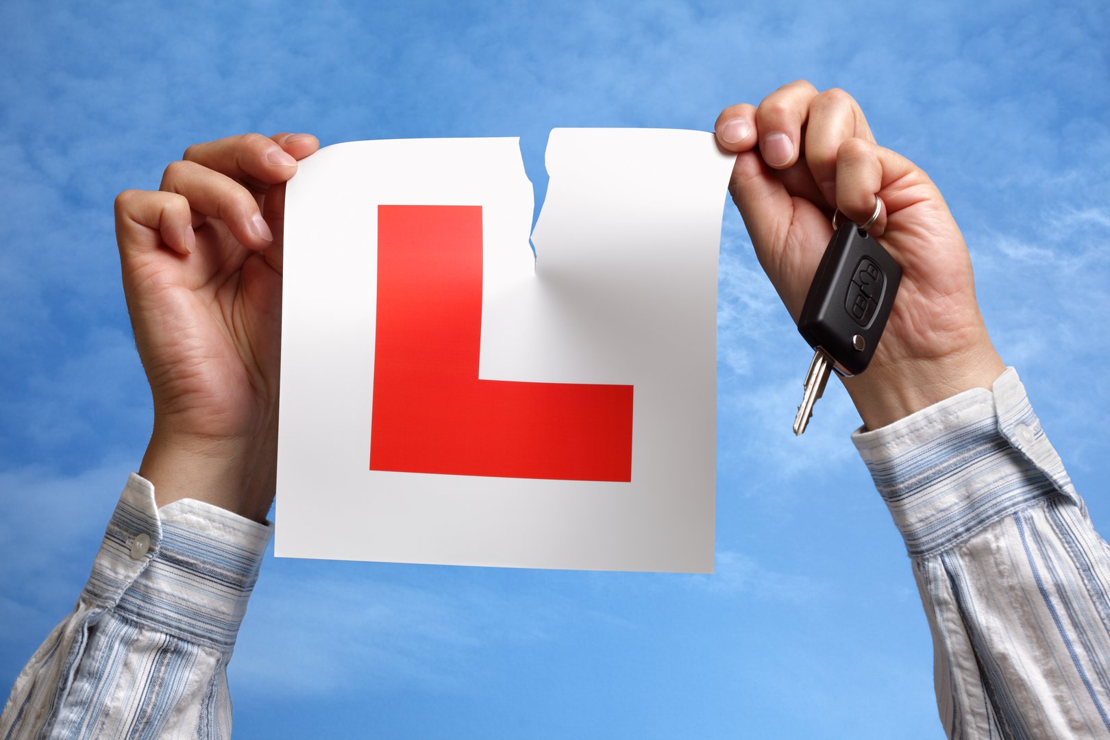 Tearing L plate against a sky holding a car key after passing driving test