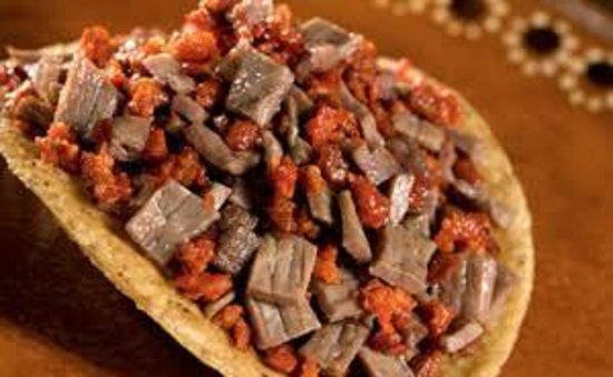 Close-up of a tostada topped with diced beef and chorizo on a rustic plate.