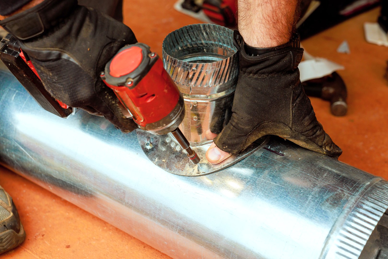 Technical worker in gloves works on attaching metal duct components with using power tool in during maintenance HVAC heating systems