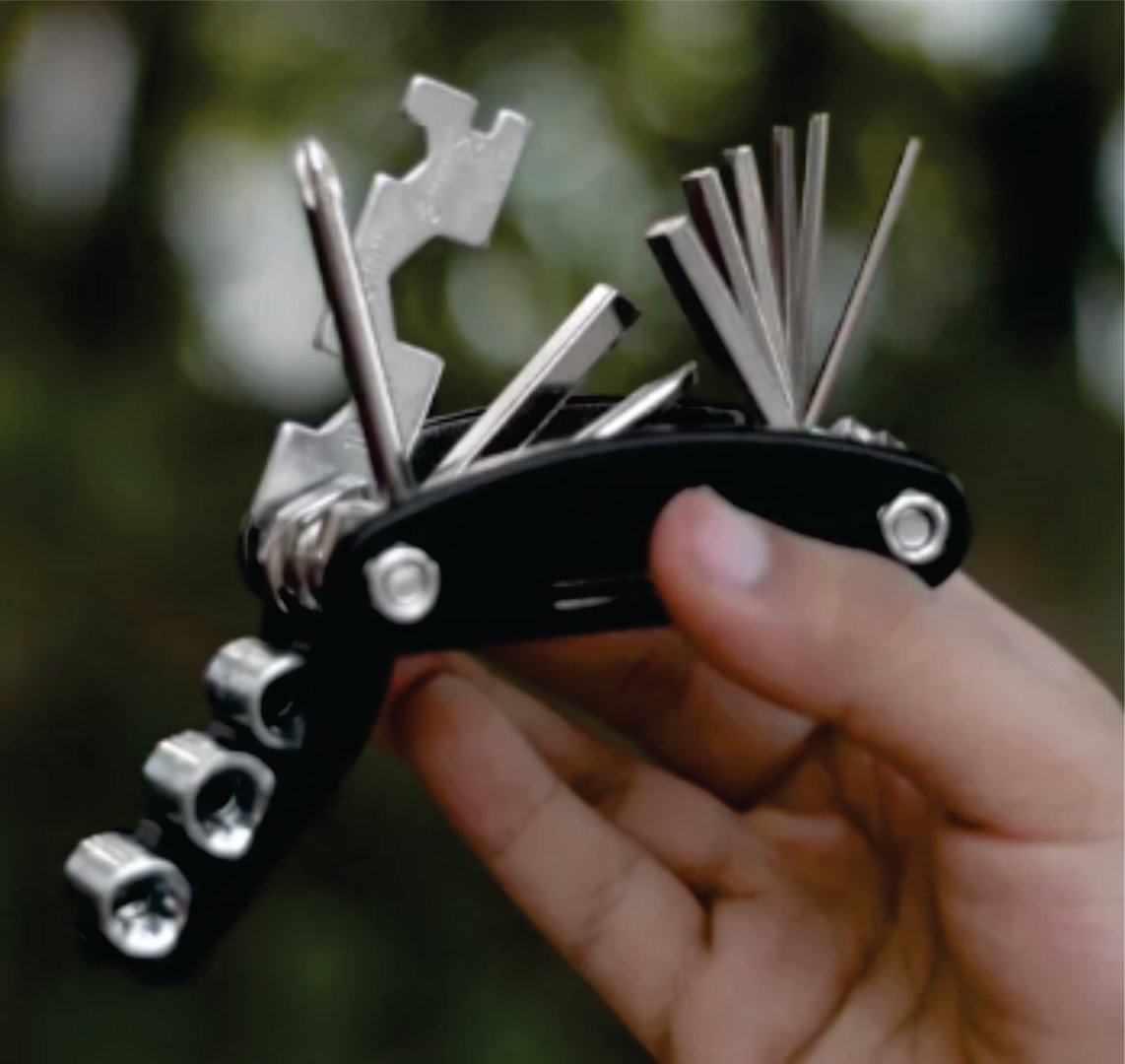 A hand holding a multi-tool with various attachments like hex wrenches and screwdrivers, set against a blurred natural background.