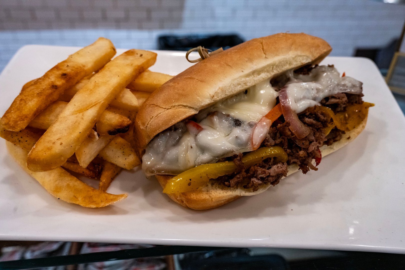 A Philly cheesesteak sandwich with provolone cheese and peppers and onions with a side of steak fries