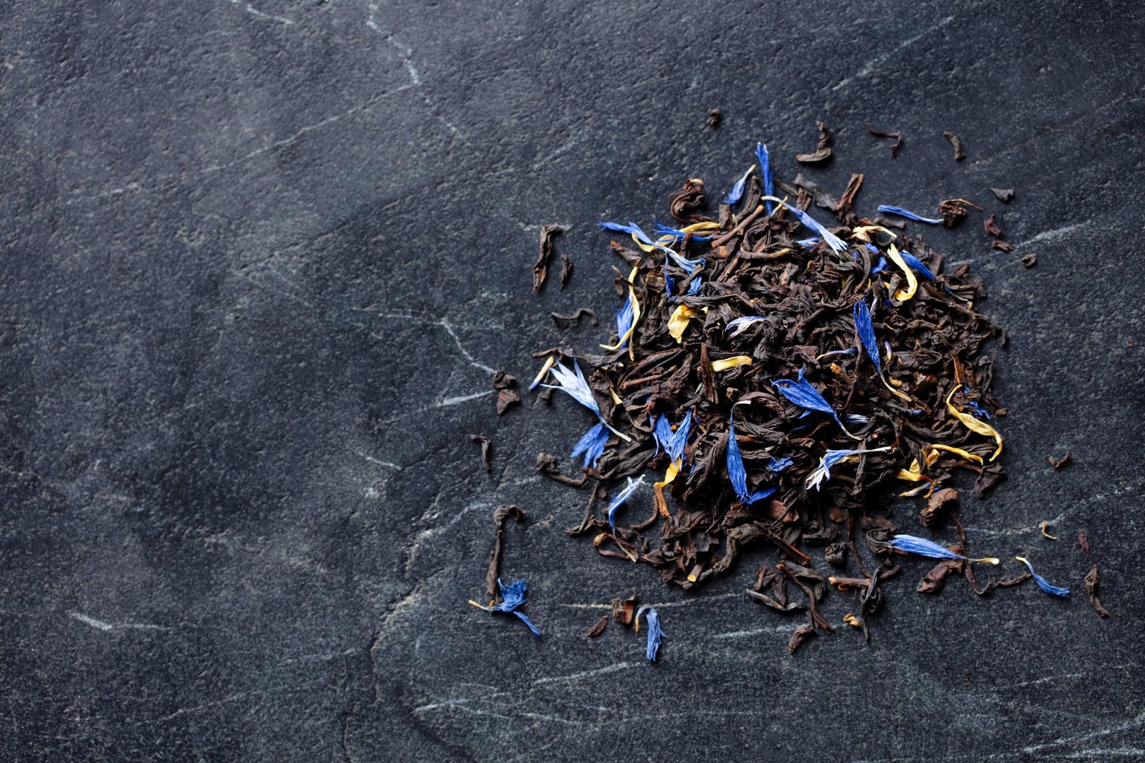 Earl grey loose leaf tea blend with cornflower and orange blossom petals. Marble background. Copy space. Top view.