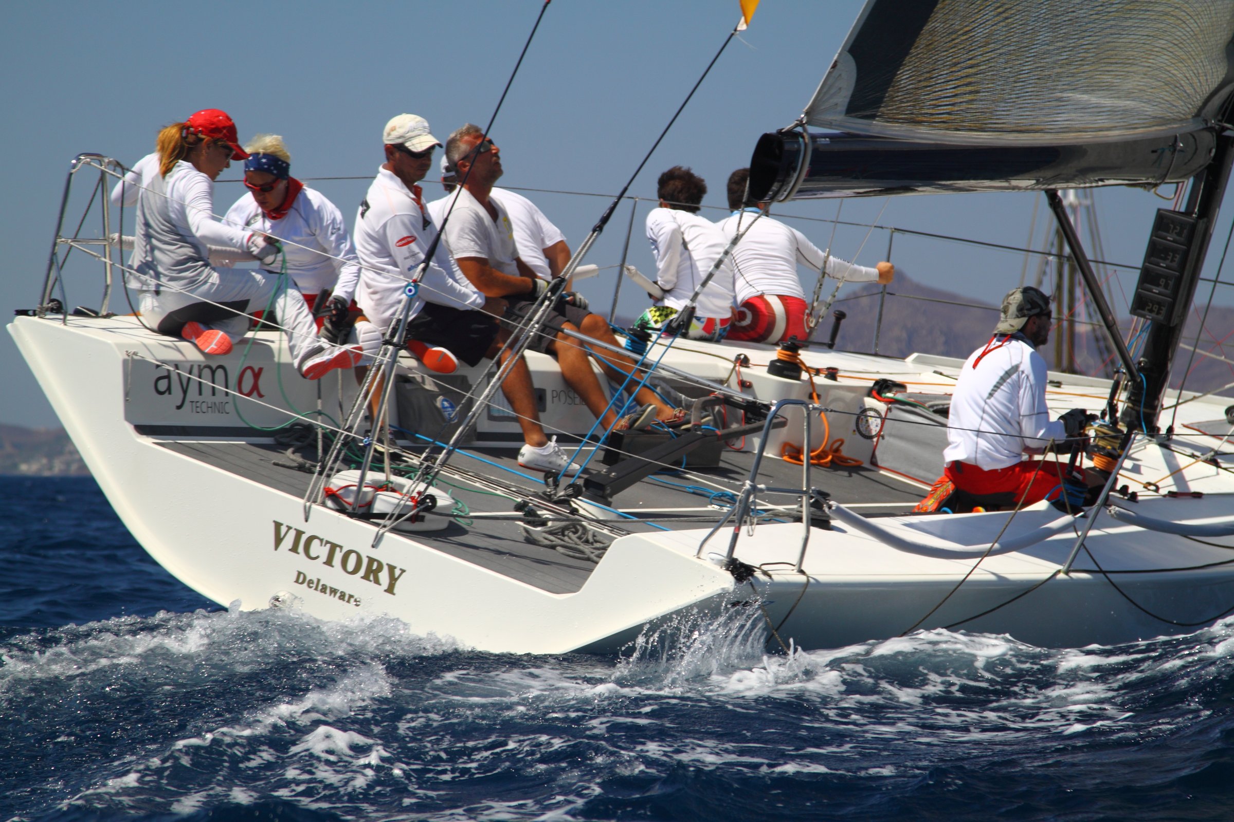 Bodrum,Turkey. 19 August 2016: sailor team driving sail boat in motion, sailboat wheeling with water splashes, mountains and seascape on background