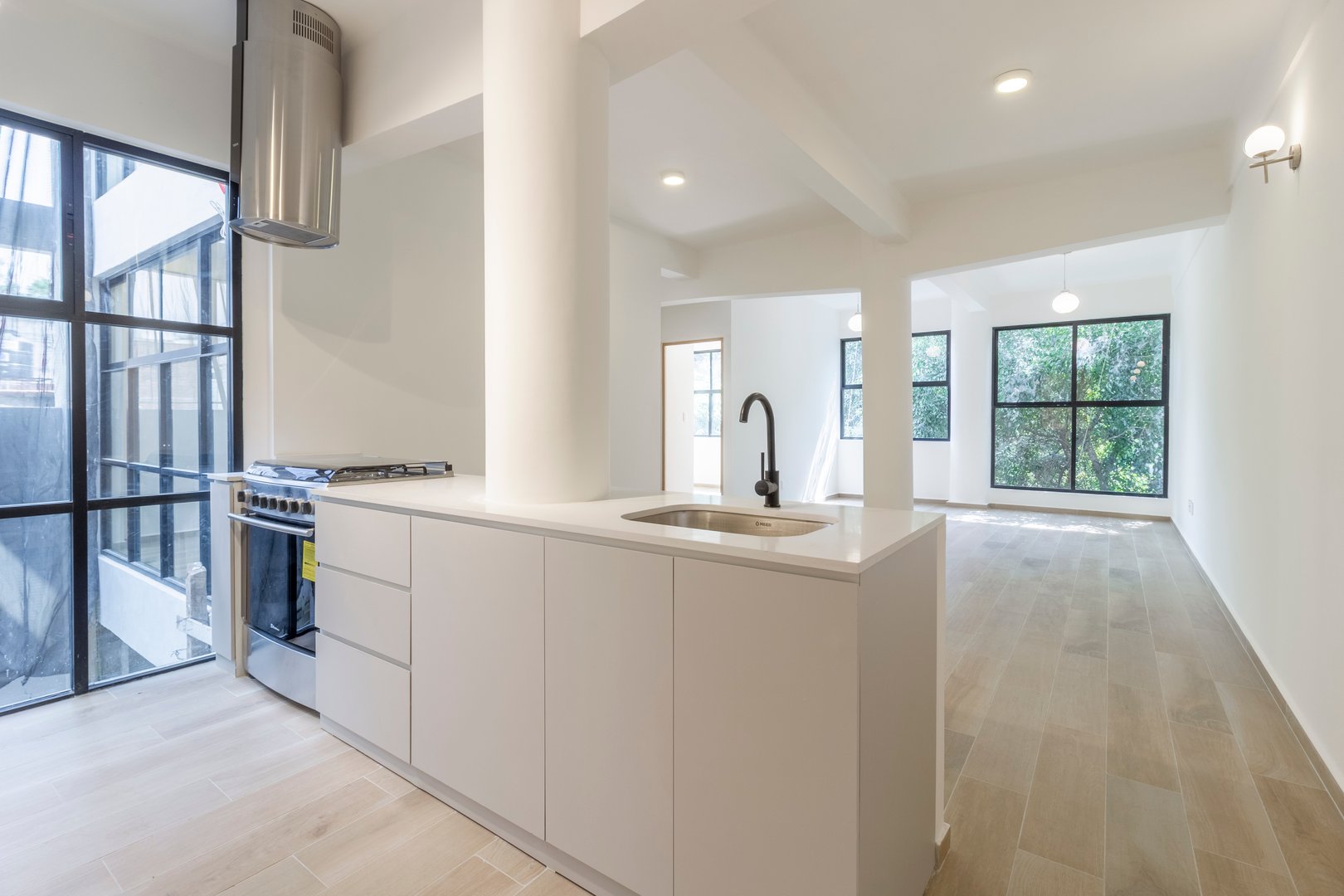 Modern open-plan kitchen and living area with large windows, light wood flooring, and white cabinetry.
