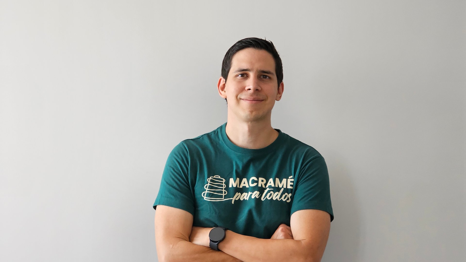 Man in a teal T-shirt with crossed arms, smiling against a gray background.