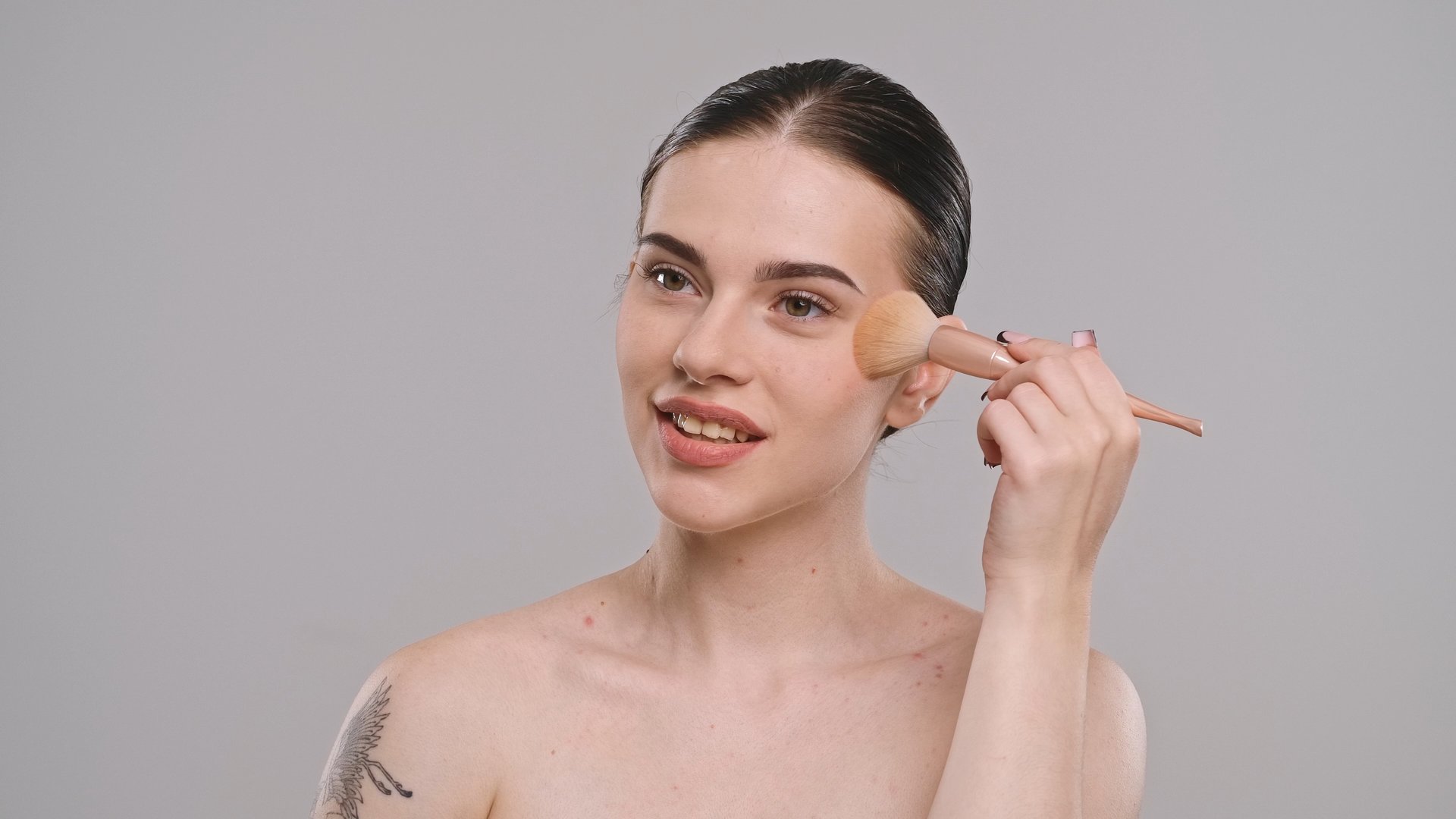 A young woman gently applies makeup with a brush to her cheeks, enhancing her natural beauty with precision and grace.