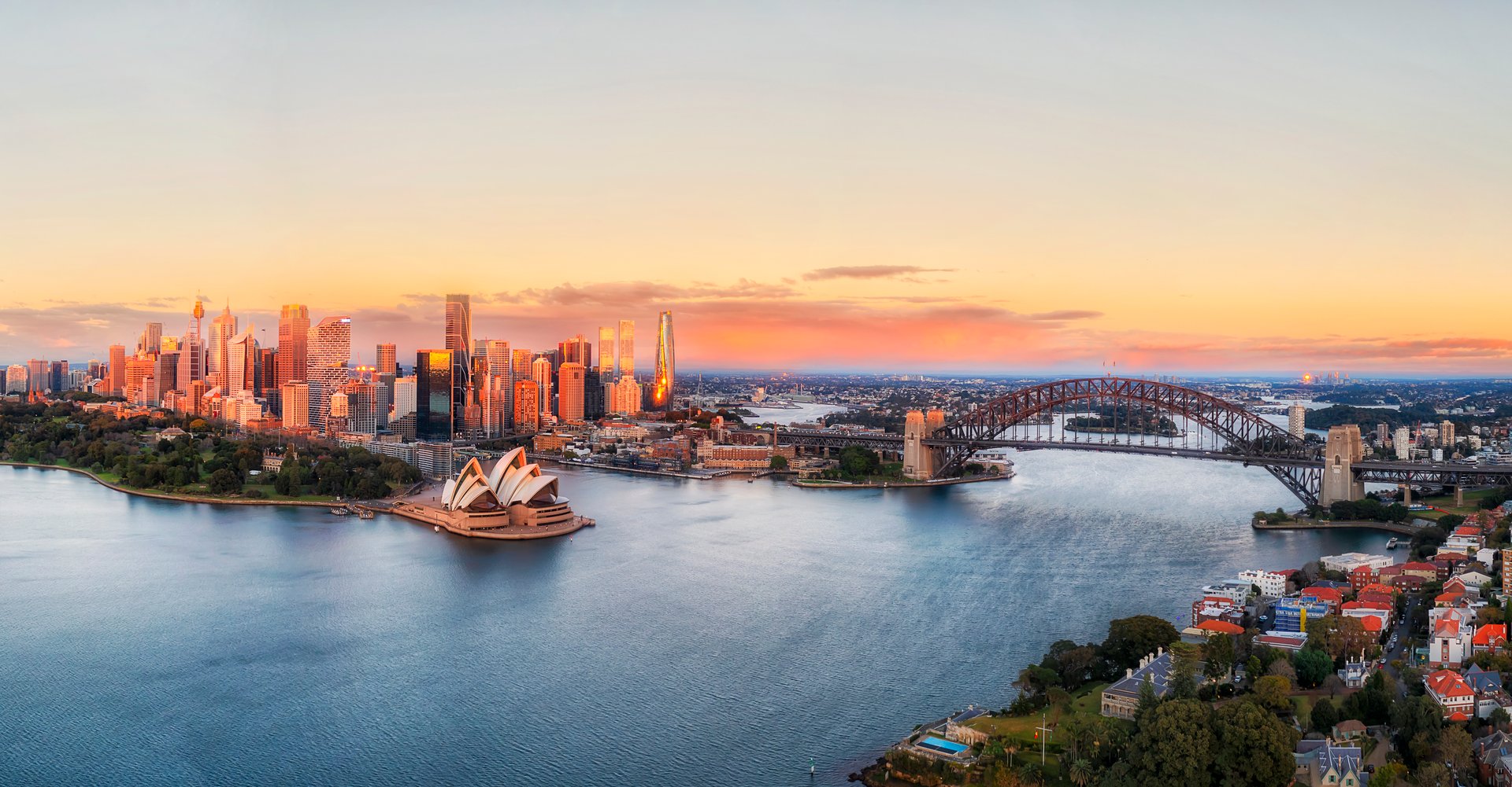 Close scenic aerial sunrise cityscape panorama of City of Sydney waterfront on shores of harbour by the Bridge.