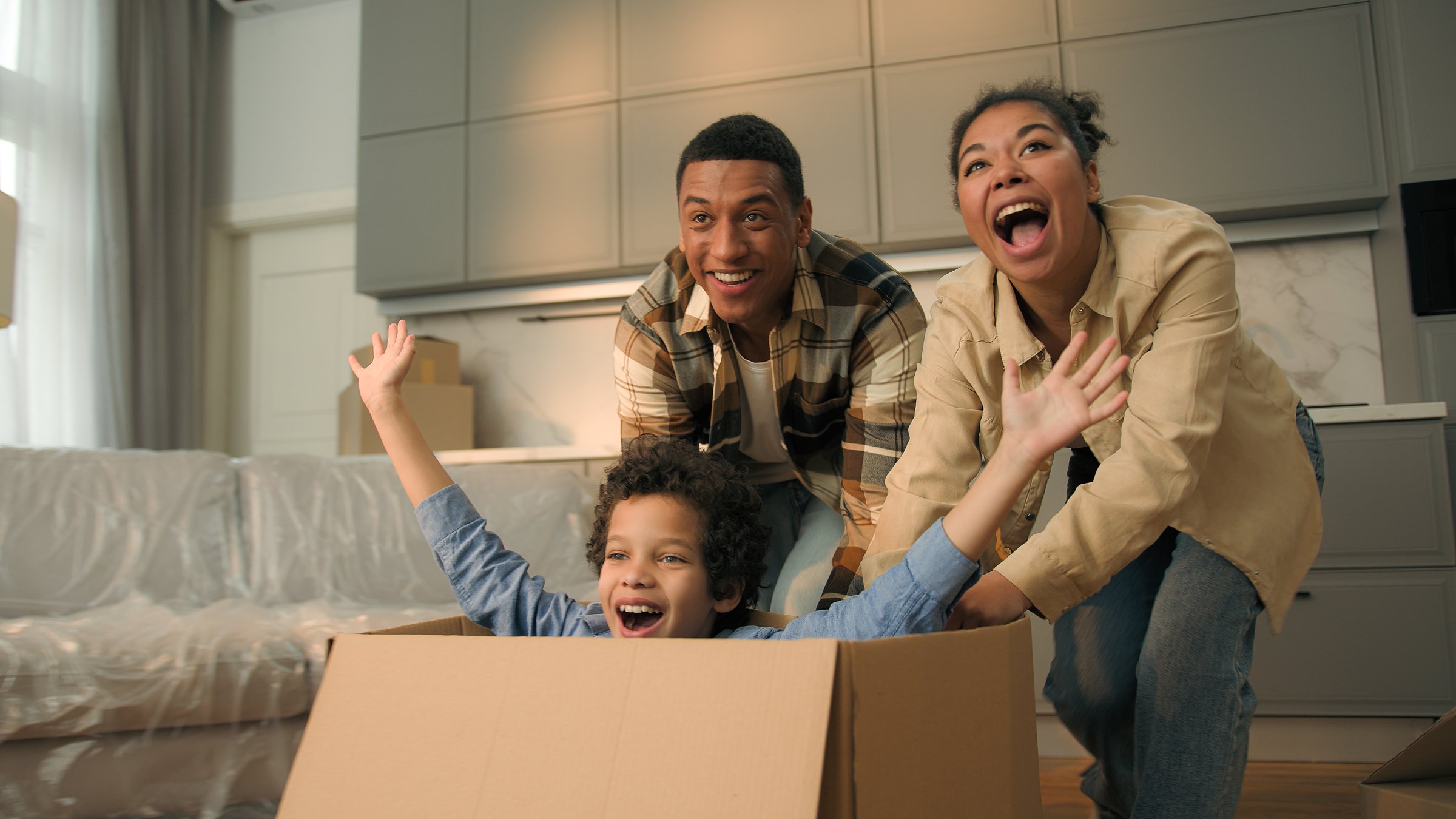 Happy African American family celebrate relocation new home joyful mother father run push cardboard box with little child boy kid ride inside cheerful parents son playing fun moving day loan mortgage. High quality 4k footage