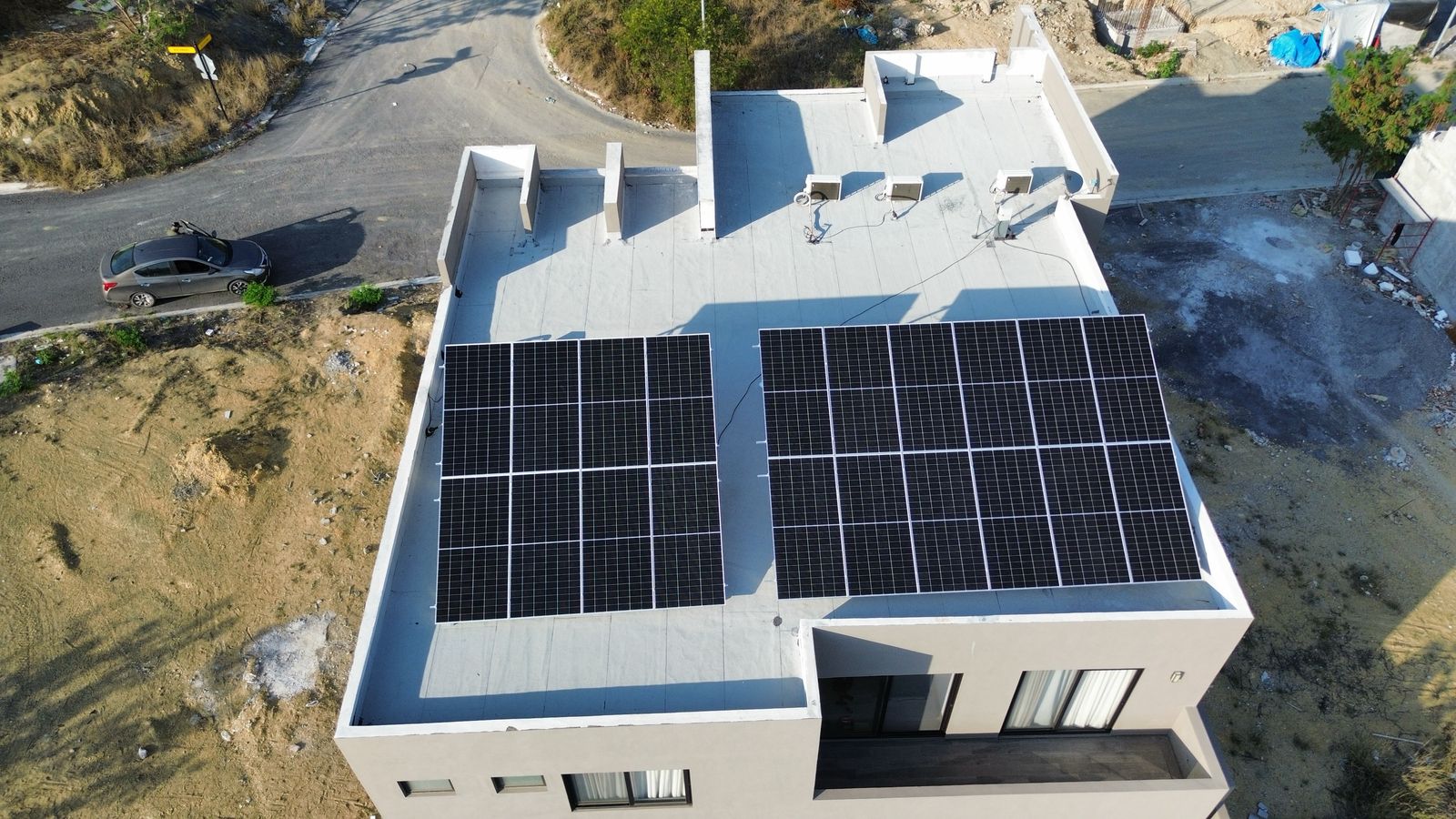 Aerial view of a flat-roofed building with large solar panels, surrounded by roads and vegetation.
