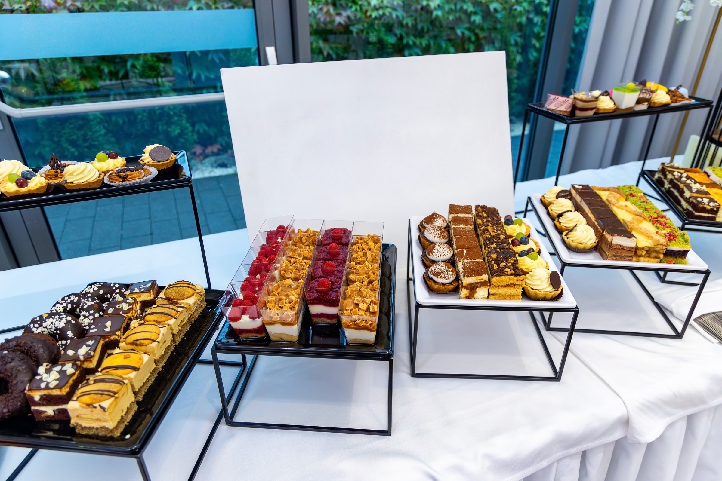 Elegant dessert buffet with assorted mini cakes. Luxurious dessert buffet table featuring a wide variety of mini cakes, tarts, mousse cups, and pastries arranged on tiered stands