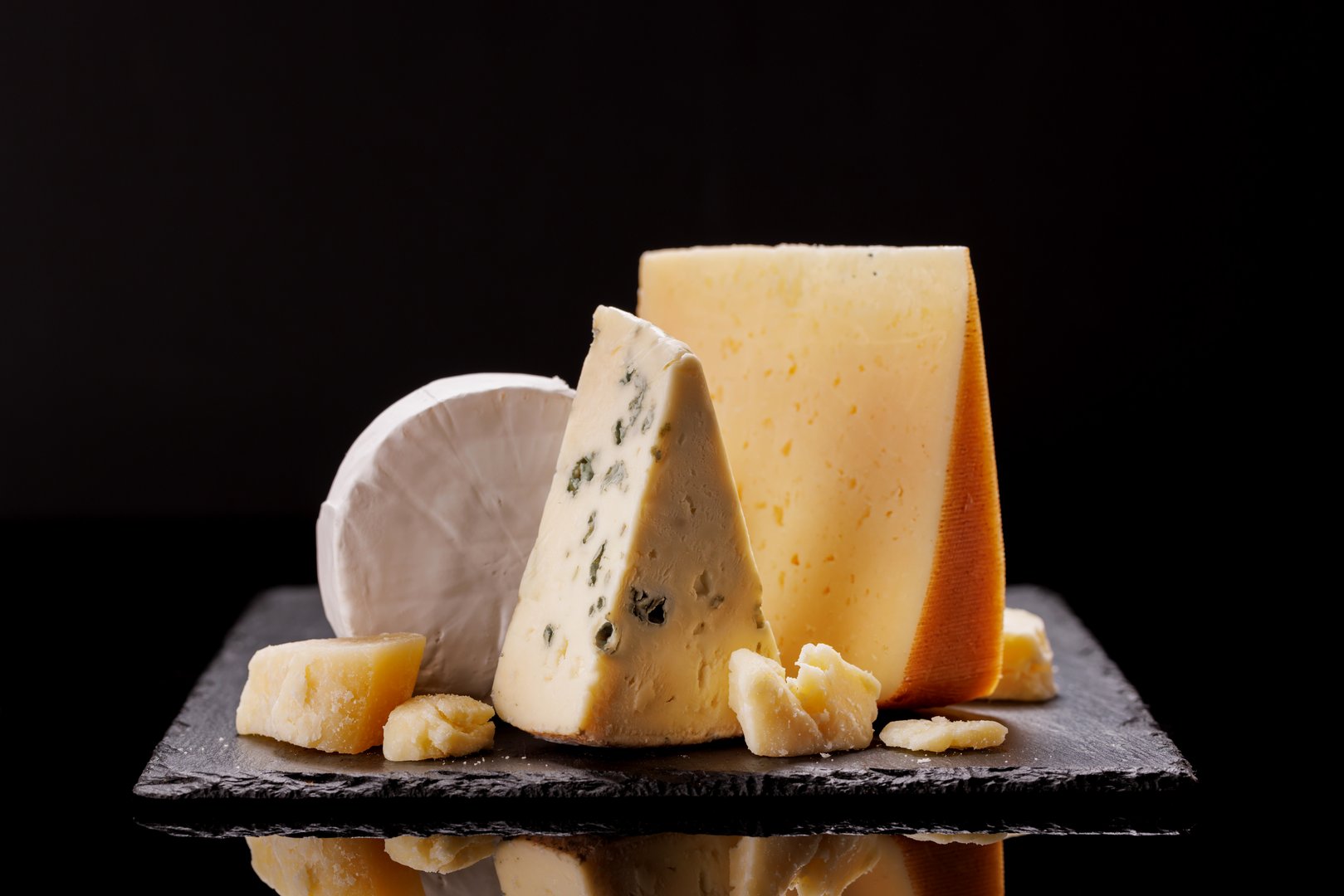 A refined selection of aged cheeses presented on a board, set against a dramatic dark background. A perfect setting for a gourmet indulgence