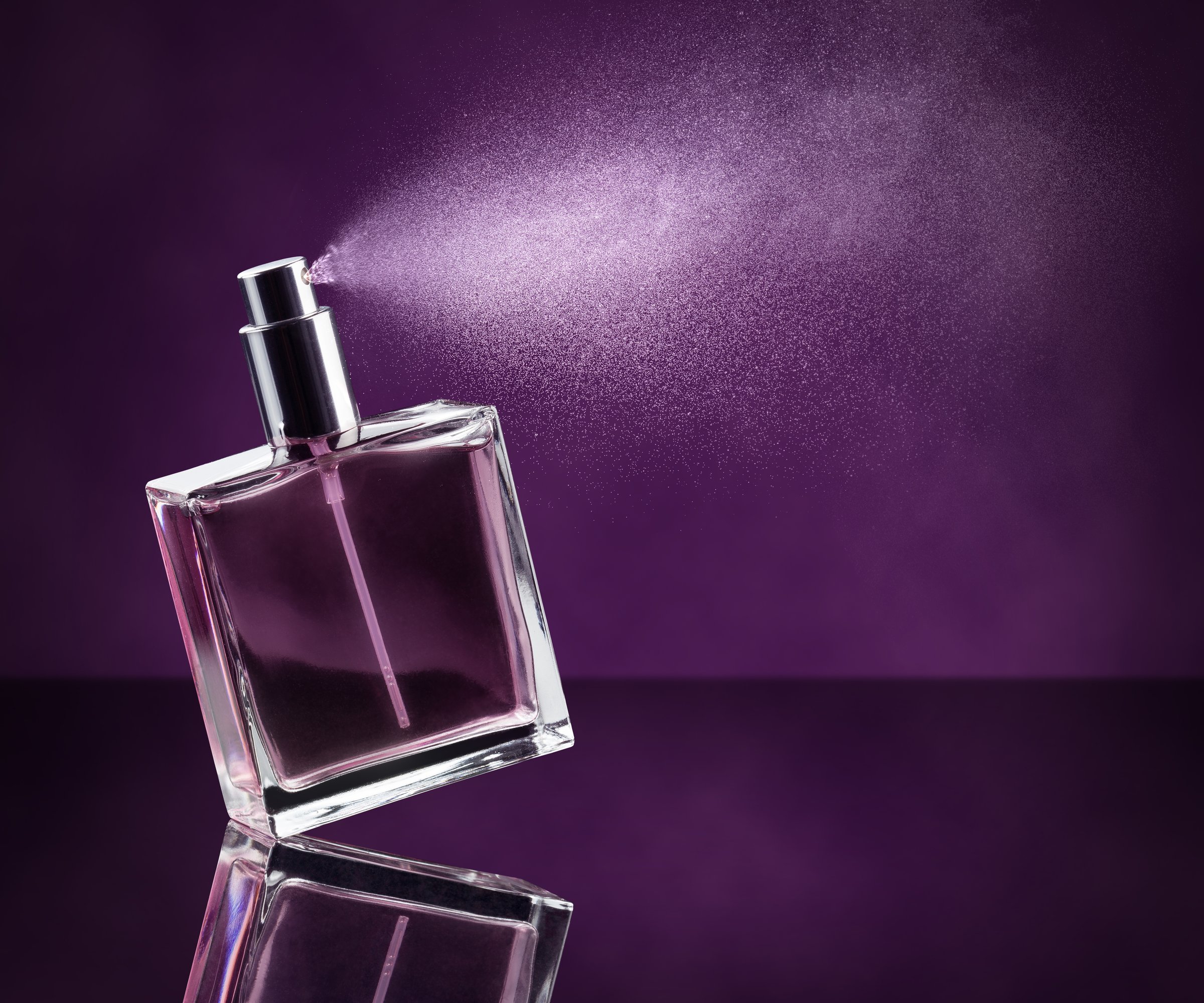 perfume bottle spraying on dark purple background