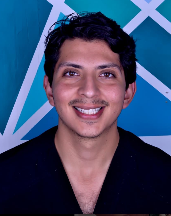 Man smiling in front of a geometric blue background, wearing a dark shirt.