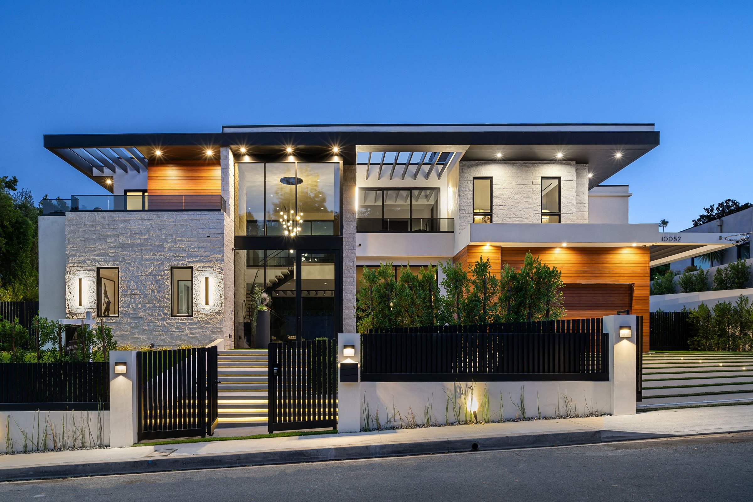 Modern luxury house exterior with large windows and contemporary design, illuminated at dusk.