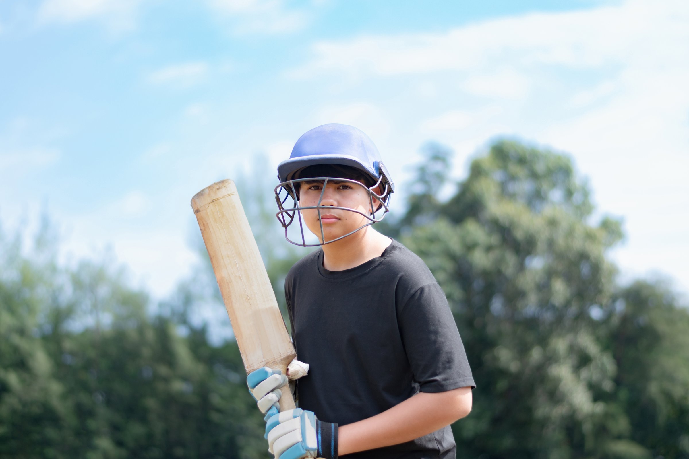 Asian boy wears helmet and gloves holding cricket bat standing to hit the cricket ball from the player during sport lesson at school.