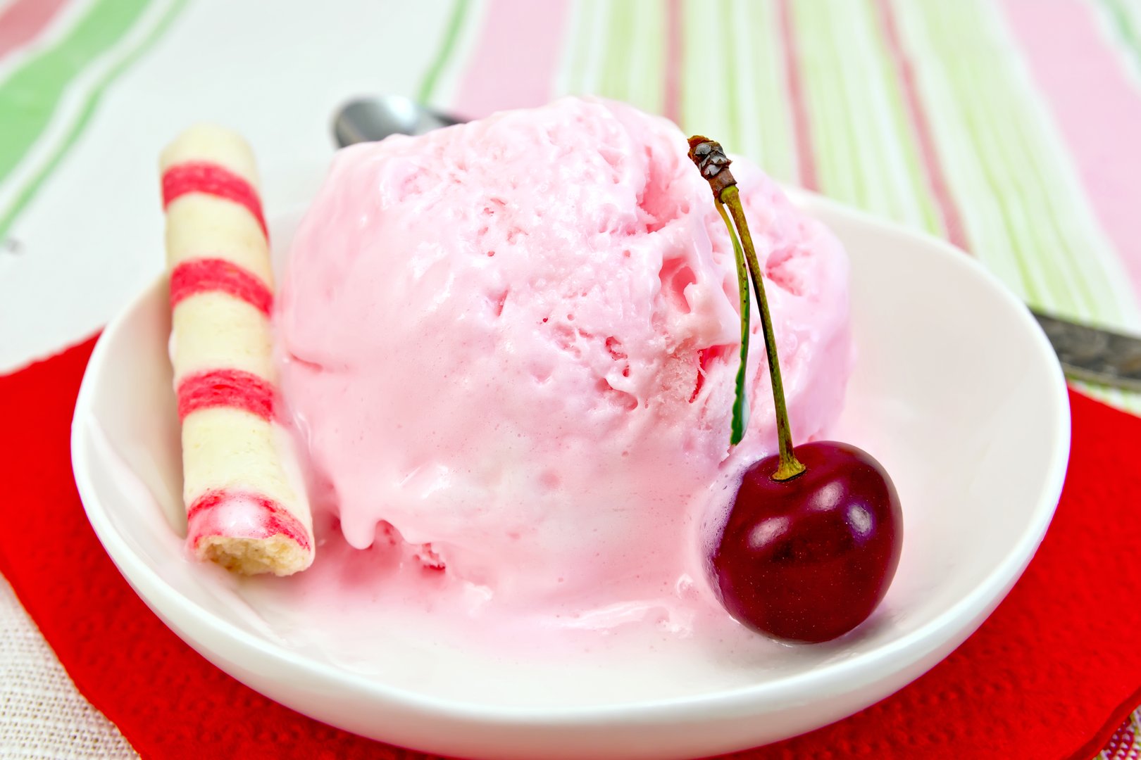 Cherry ice cream in a bowl with wafer rolls on a red paper napkin, spoon on a background of a linen tablecloth