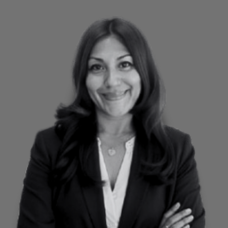 Smiling woman with long hair wearing a blazer and white blouse, arms crossed in front of a gray background.