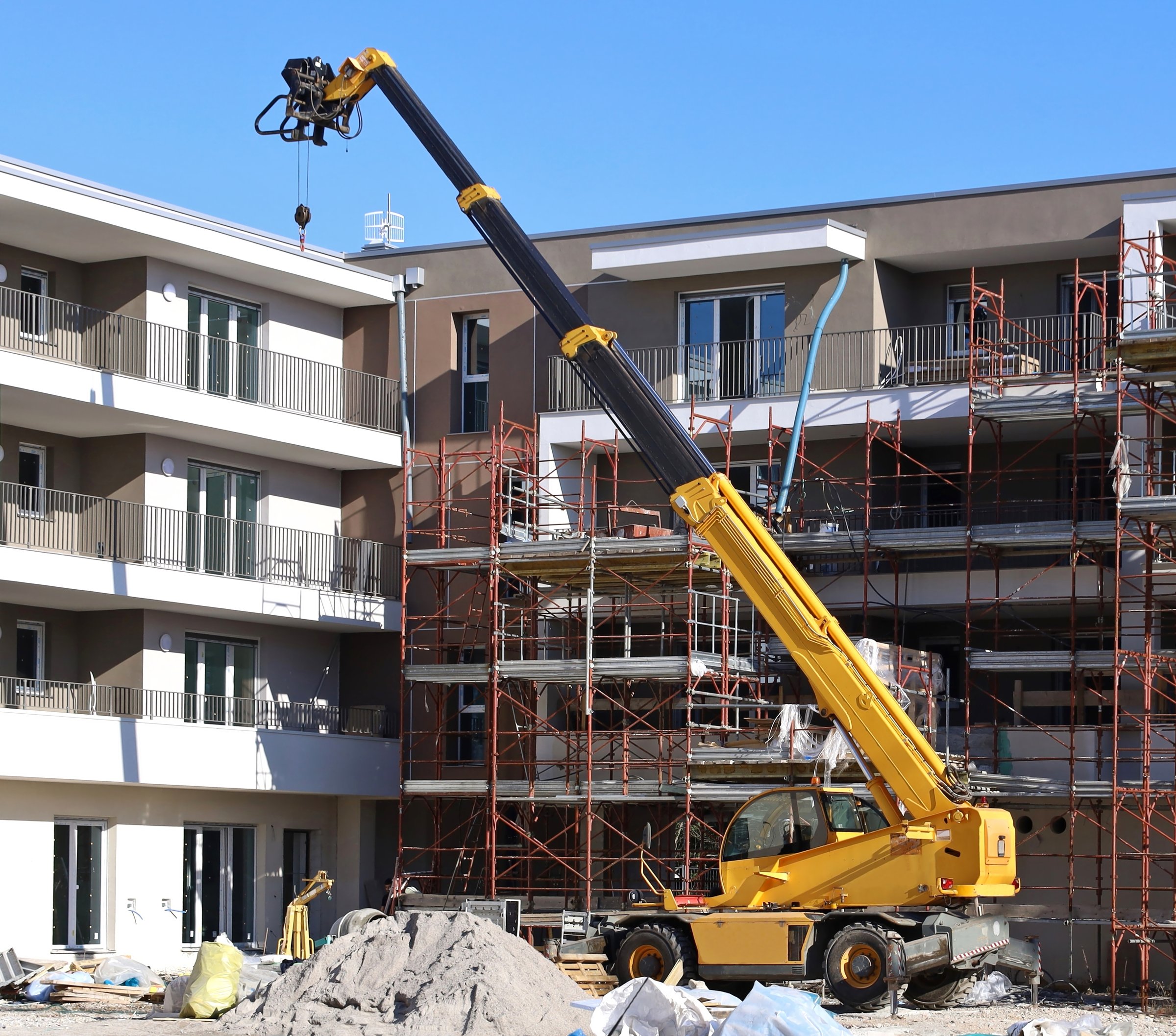 Yellow rotating telehandler at work in front of two new building under construction.