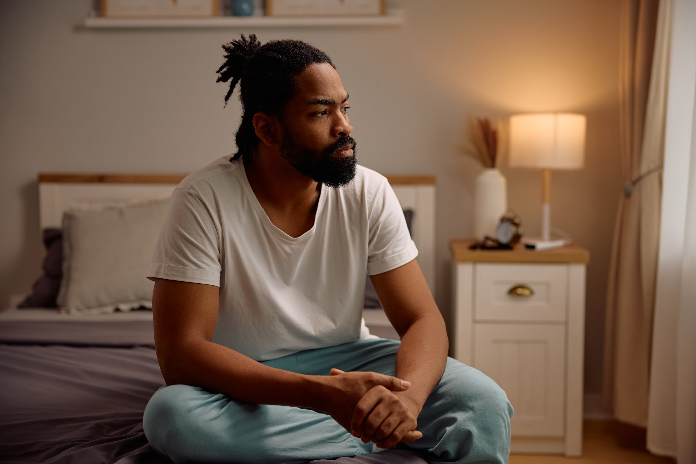 Thoughtful African American man sitting on a bed. Copy space.