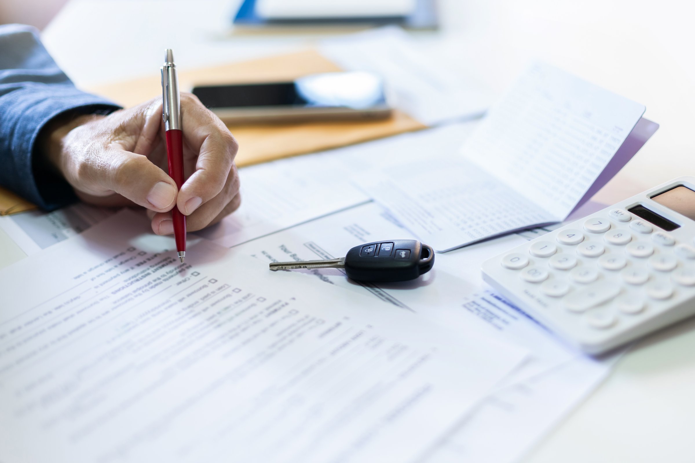 Men's hand holding pen checking personal loan contract with passbook and bank statement to apply for a loan. concept to purchase the first car