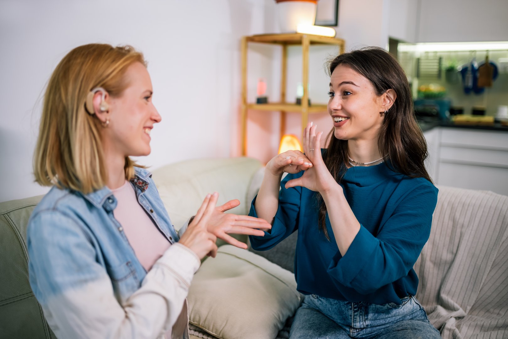 Two young girls using sign language to talk to each other. One is wearing a hearing aid. They are smiling and enjoying the conversation.