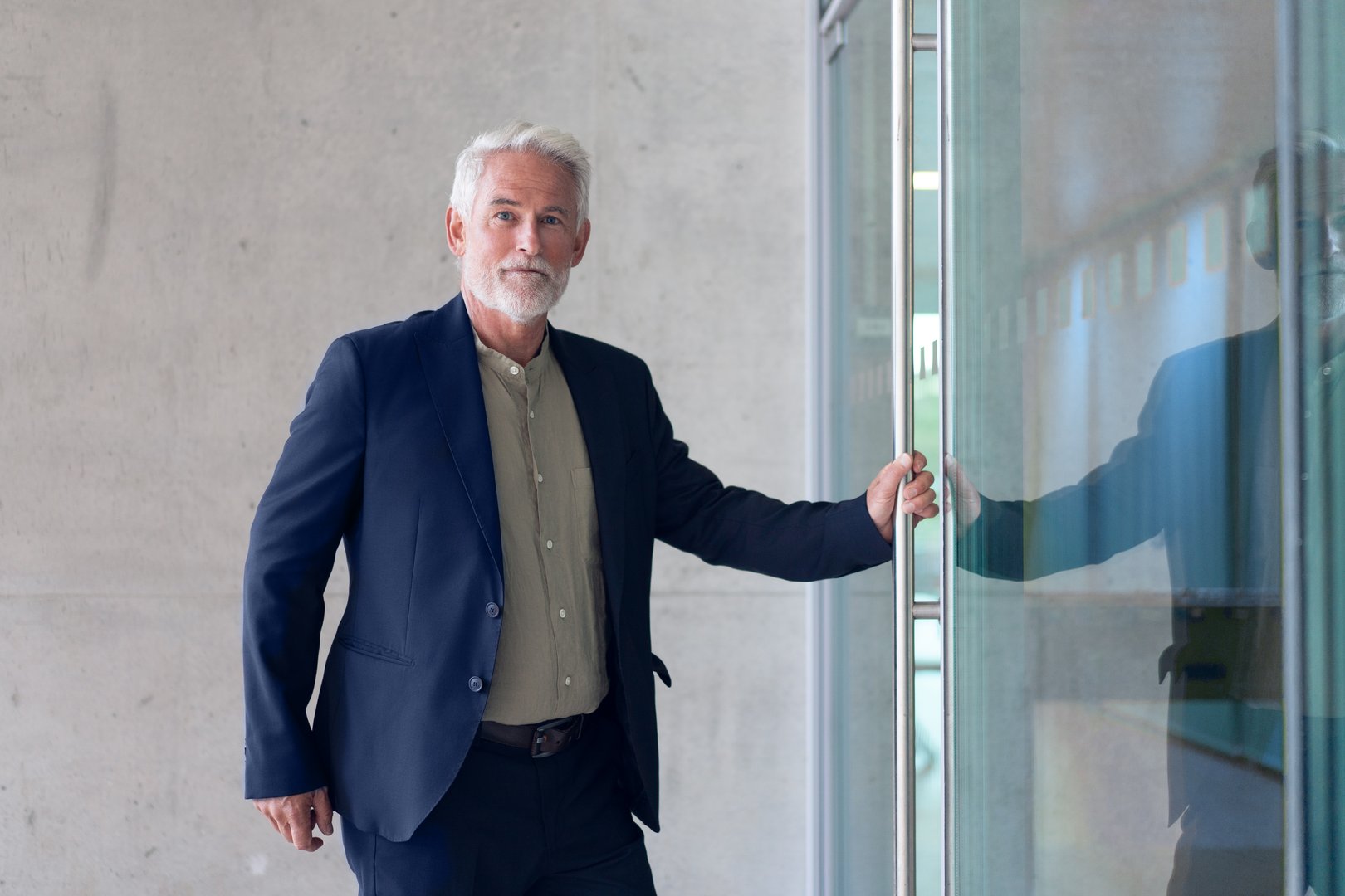 Confident senior businessman in formal attire opening glass door of modern office building. He looks professional stepping into contemporary workplace