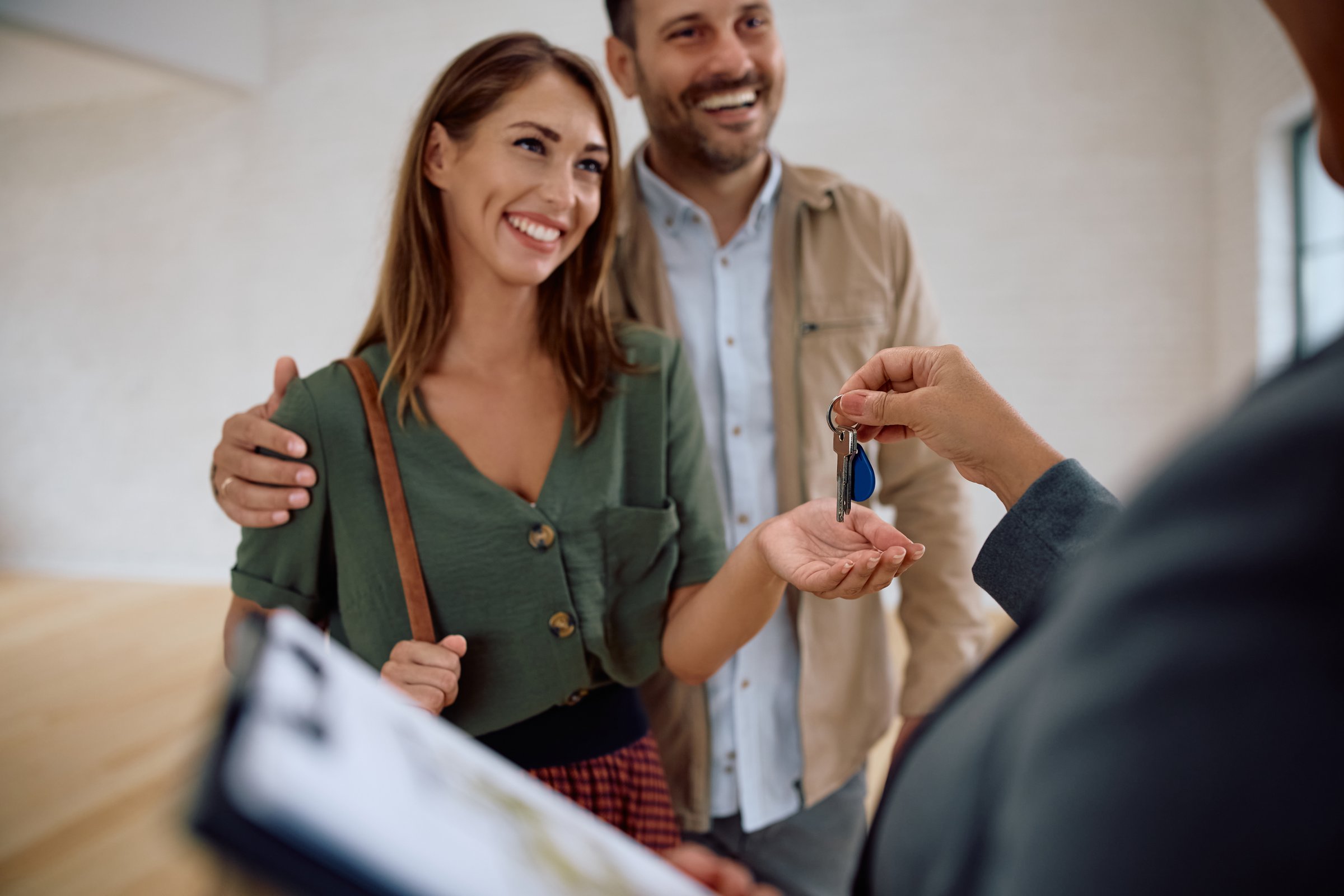 Happy couple receiving keys of their new home from real estate agent. Focus is on woman.