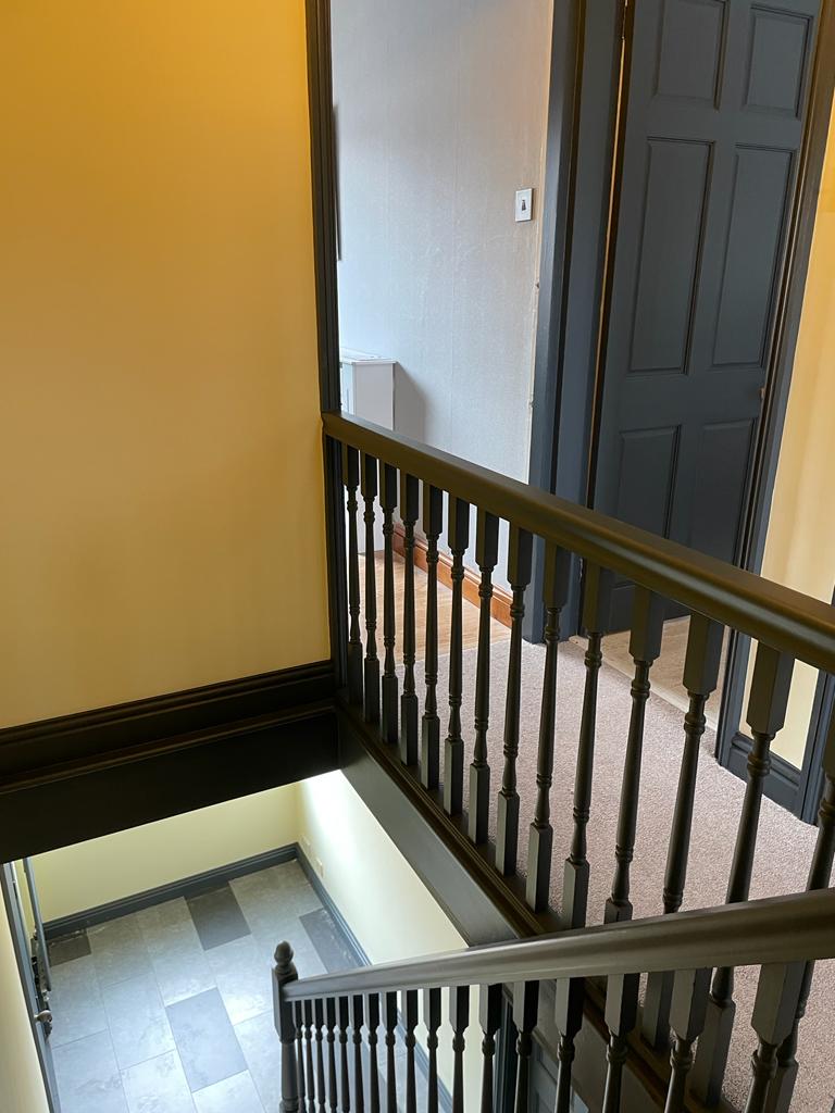 Interior view of a staircase with dark wood railings and doors, surrounded by yellow walls and a tiled floor.