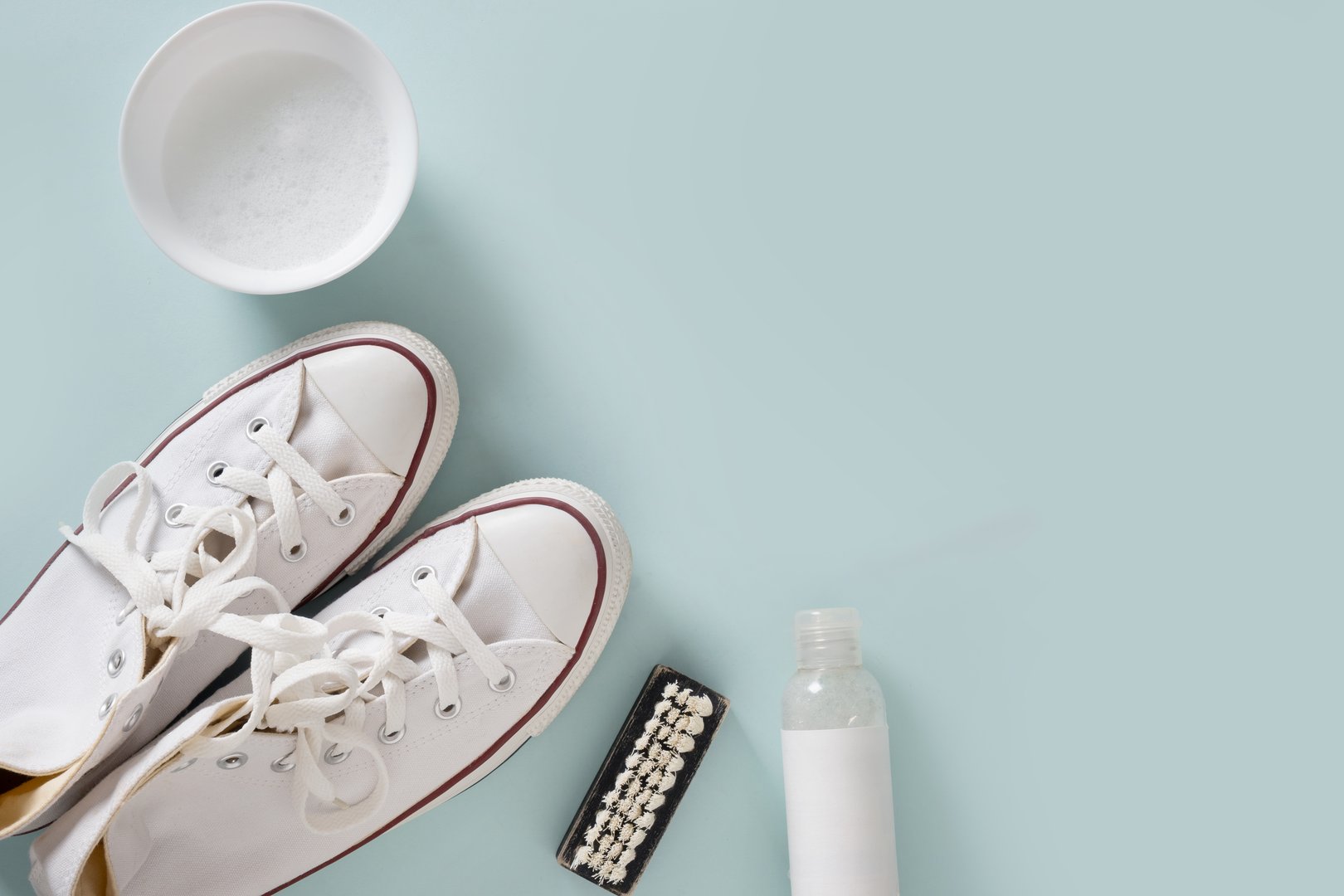 Concept of cleaning and washing white shoes by special foam and brush on blue background. Washing and cleaning concept. View from above.