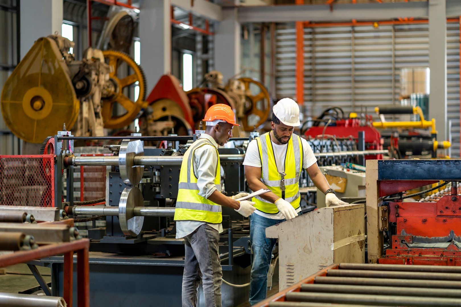 Team of African American industrial worker is checking the setup value of metal sheet roll forming machine by automated monitor while working inside roof factory for safety industry