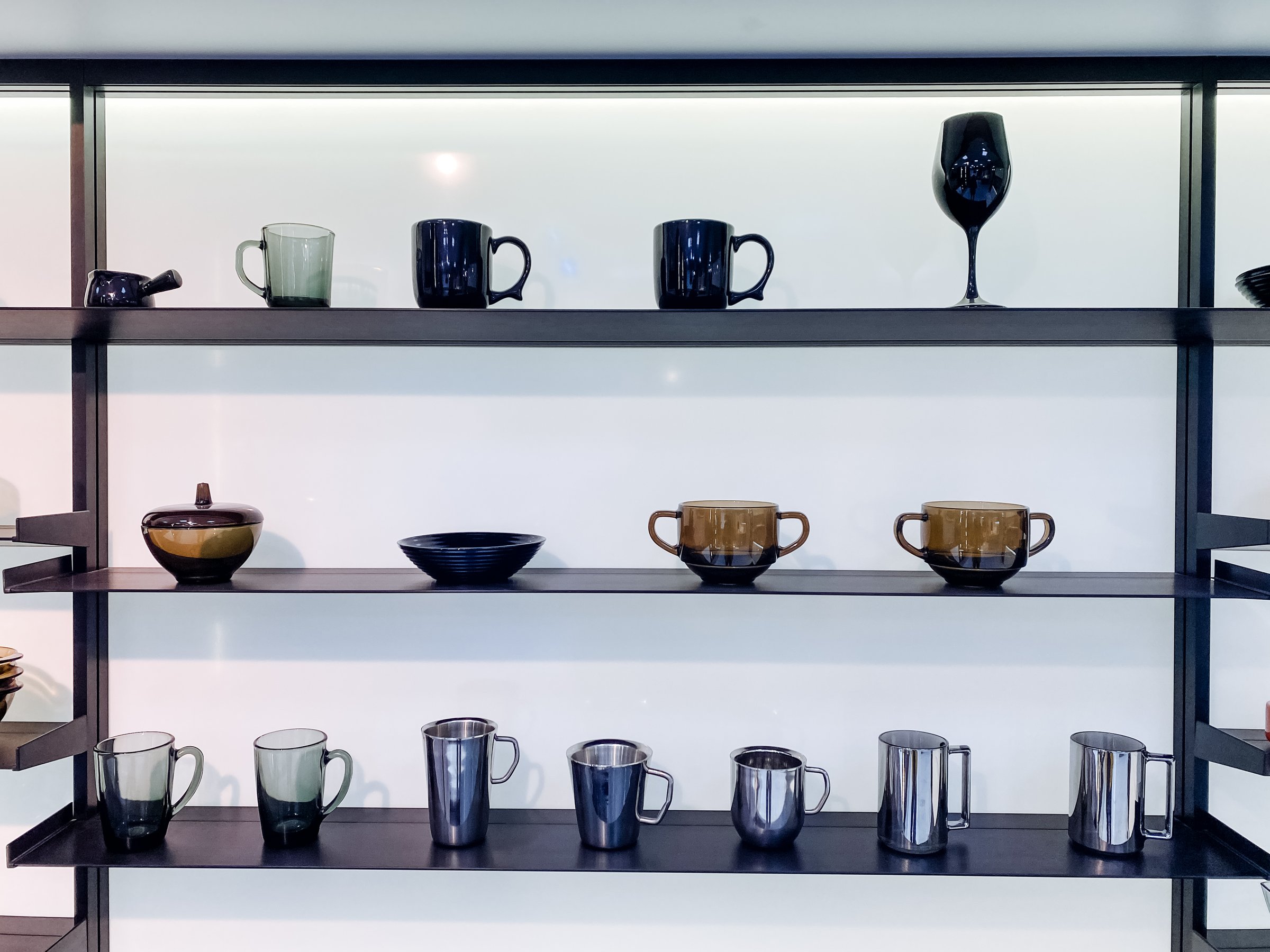A wellorganized shelf filled with an impressive assortment of cups, decorative pitchers, and elegant wine glasses, showcasing a stunning variety of tableware and serveware for all to admire
