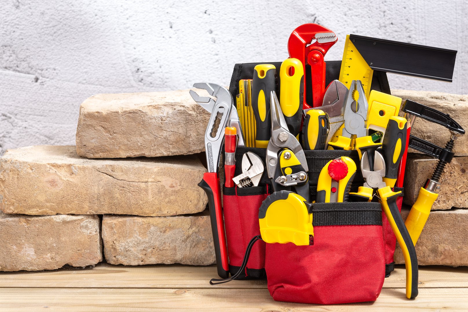 Belt bag with various hand tools leaning on an old bricks on a wooden table with copy space for text. Selective focus.