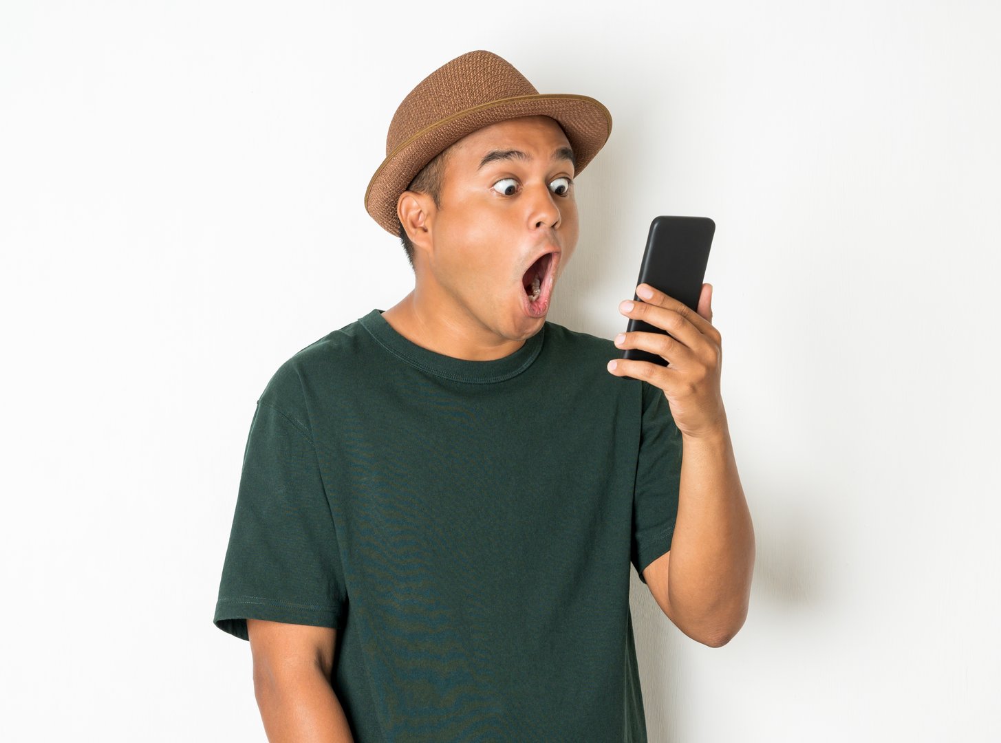 Asian men are using smartphones. He looks at the phone Then made a very surprised face He wears an old green shirt and wears a brown hat. He is around 27-35 years old.