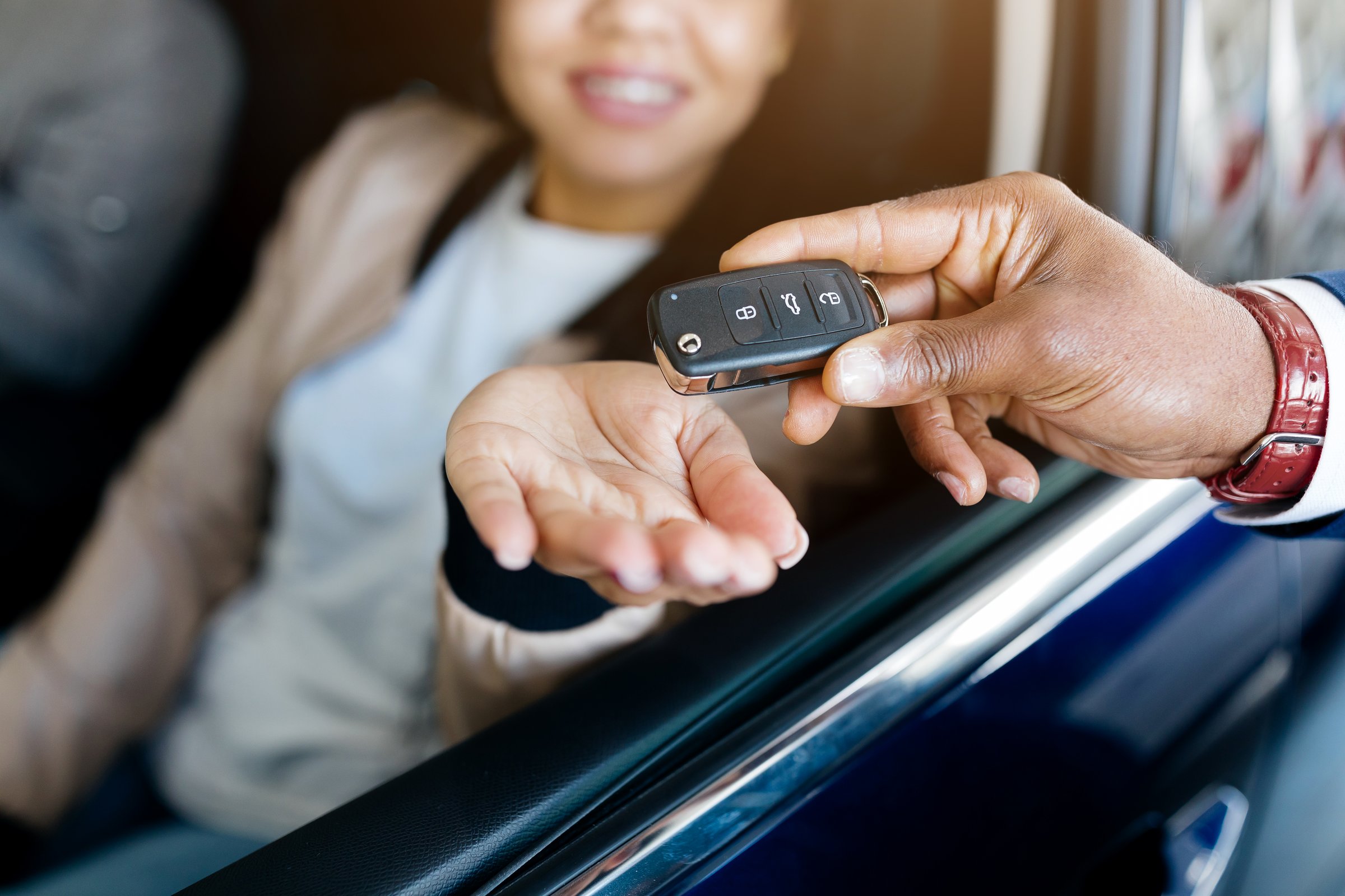 New Car. Manager giving key from automobile to happy young black lady at auto dealership store, selective focus on hand. Cheerful female customer buying vehicle from salesman seller at showroom. High quality photo