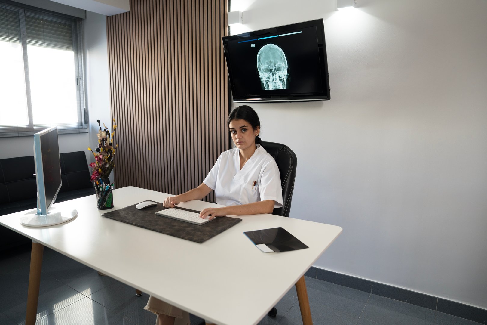 Young female medical professional sitting at her desk, with a skull x-ray on screen