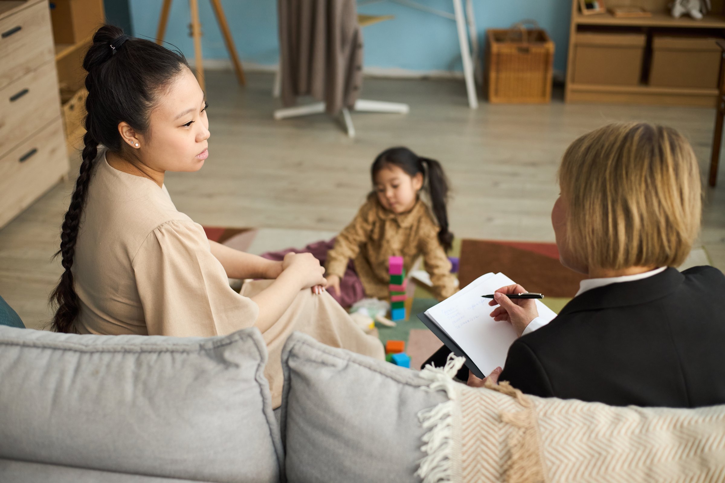 Family therapy session with therapist taking notes while child is playing with blocks in living room with casual atmosphere and open communication