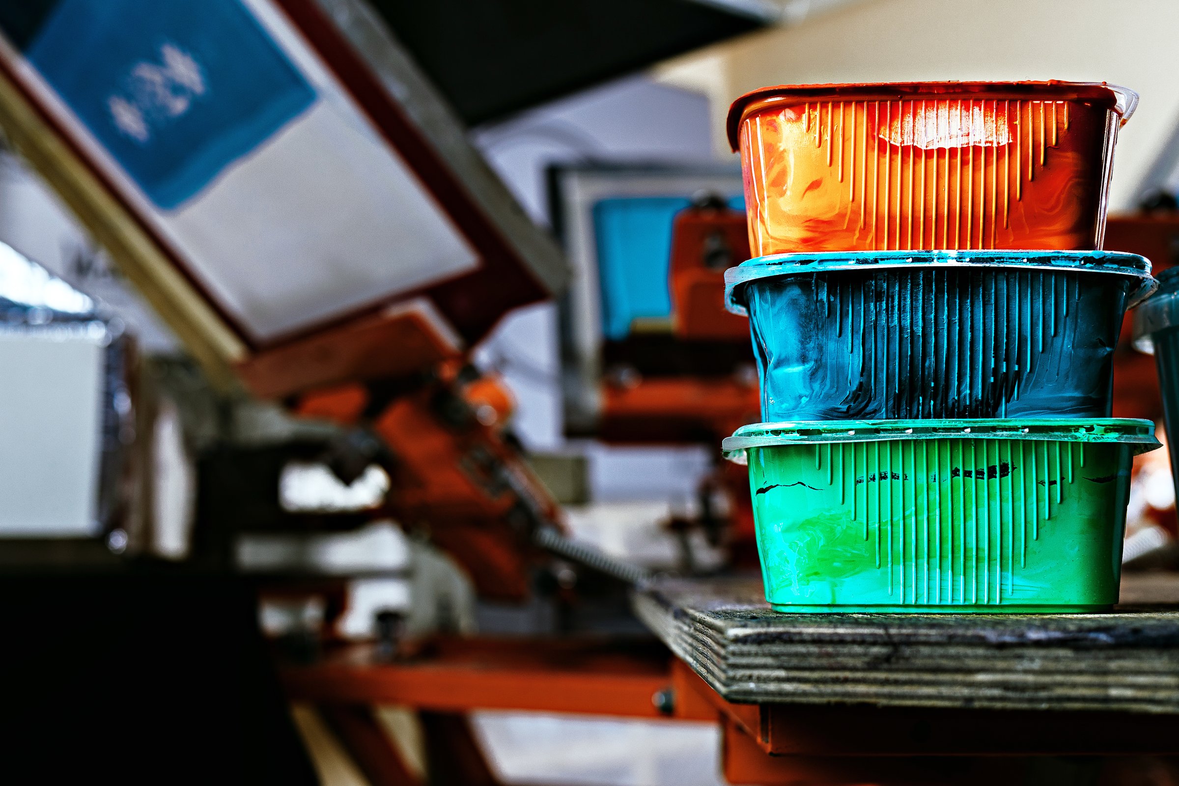 selective focus photo of various paints on wooden shelve on the print screening apparatus. serigraphy production. printing images on t-shirts